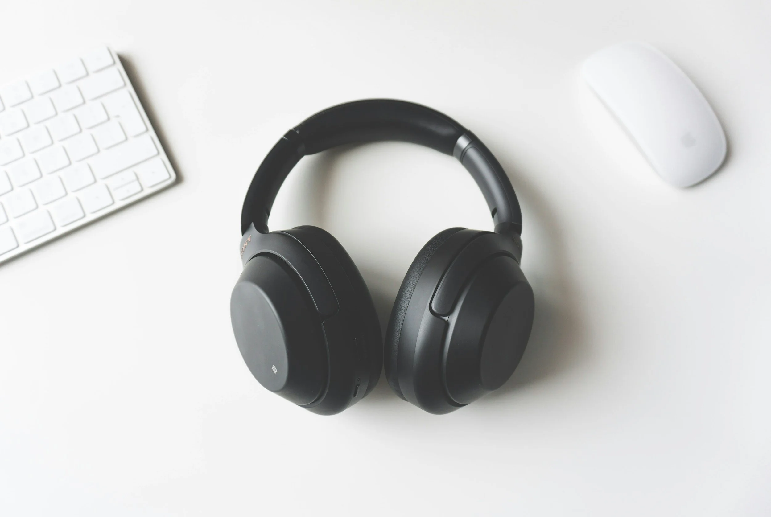 Over-ear headphones on a white desk next to a wireless keyboard and mouse.