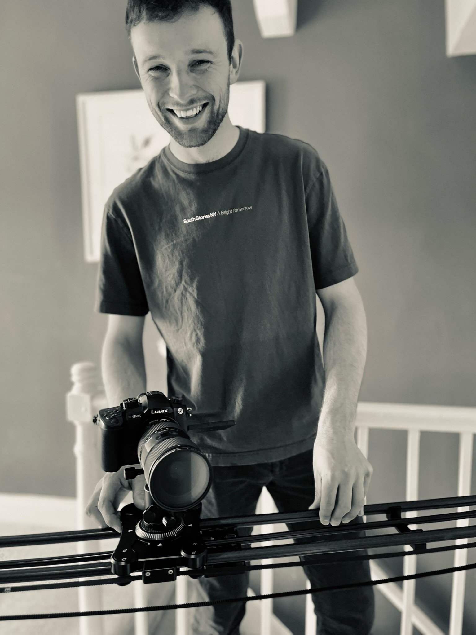 Bridge House Somerset - A man smiling, holding a camera on a slider, indoors in a room with a white crib and wall-mounted frames.