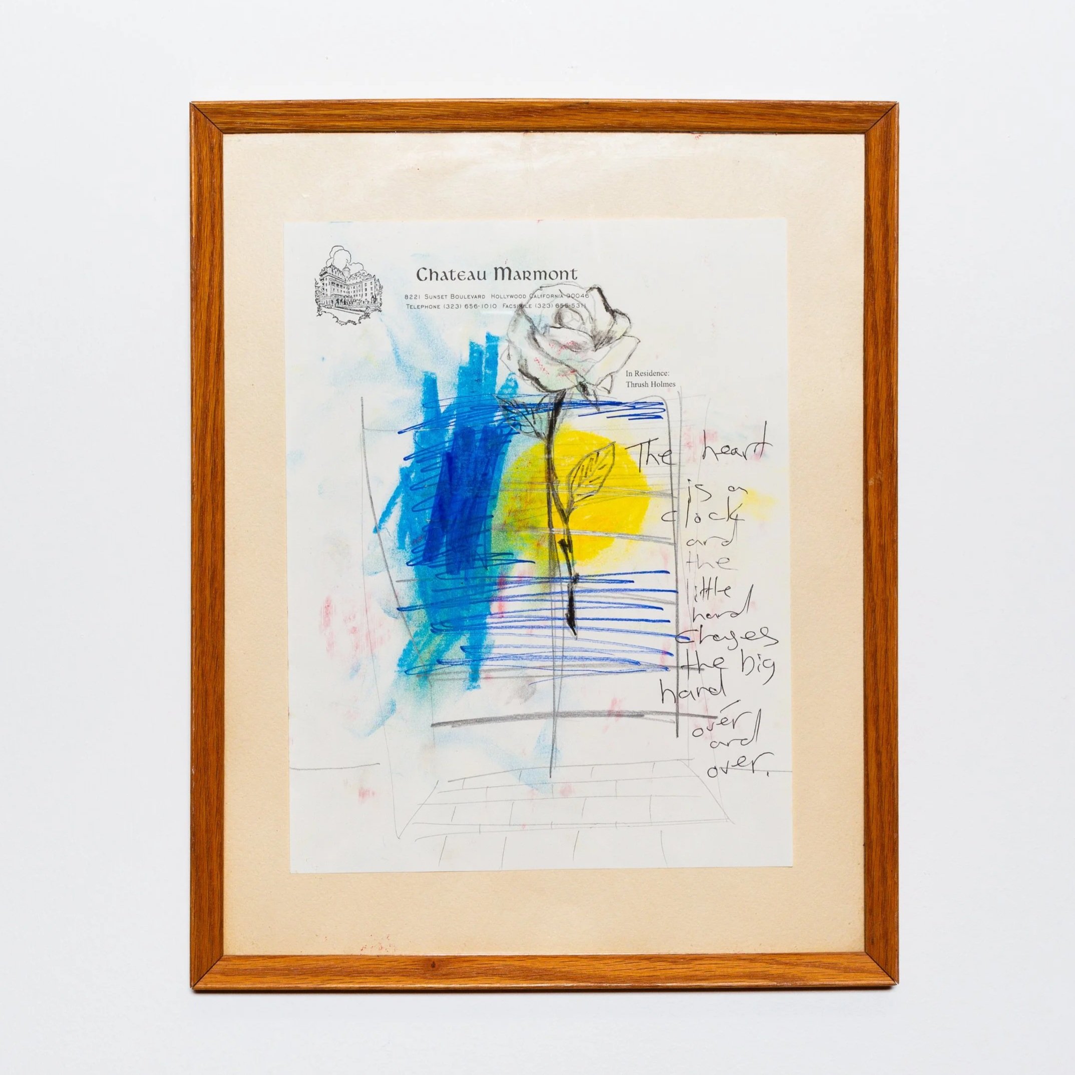 Framed artwork or note paper with drawing and handwritten text, mounted on a white wall.