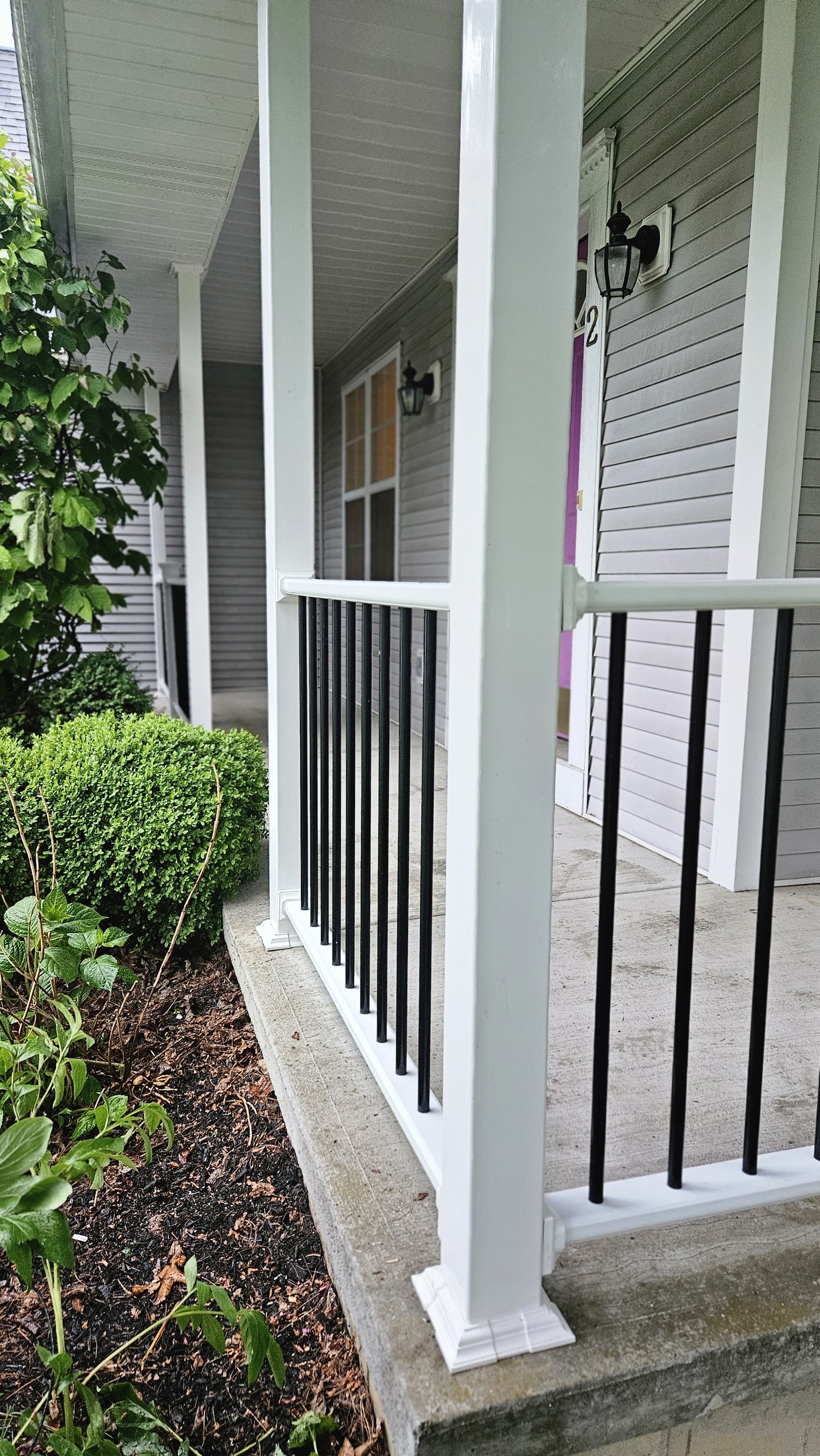 After photo showing the updated porch railings with white posts, black metal spindles, and finished trim details for a clean exterior look. 