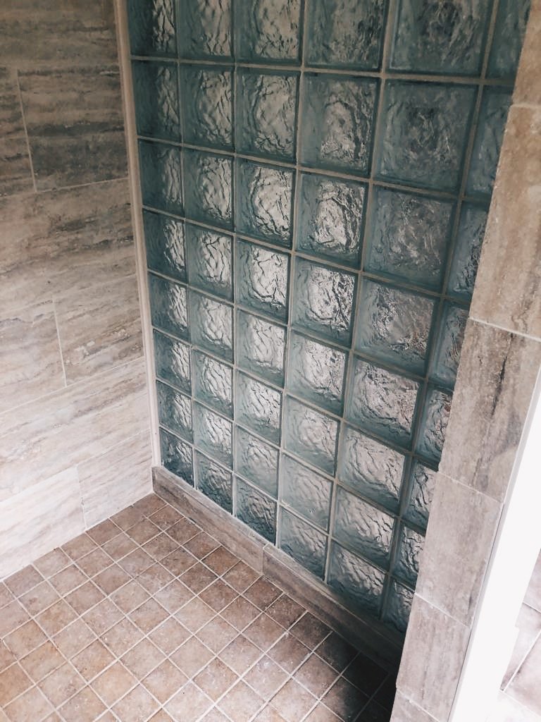 Shower area with glass block wall and brown tiled floor.