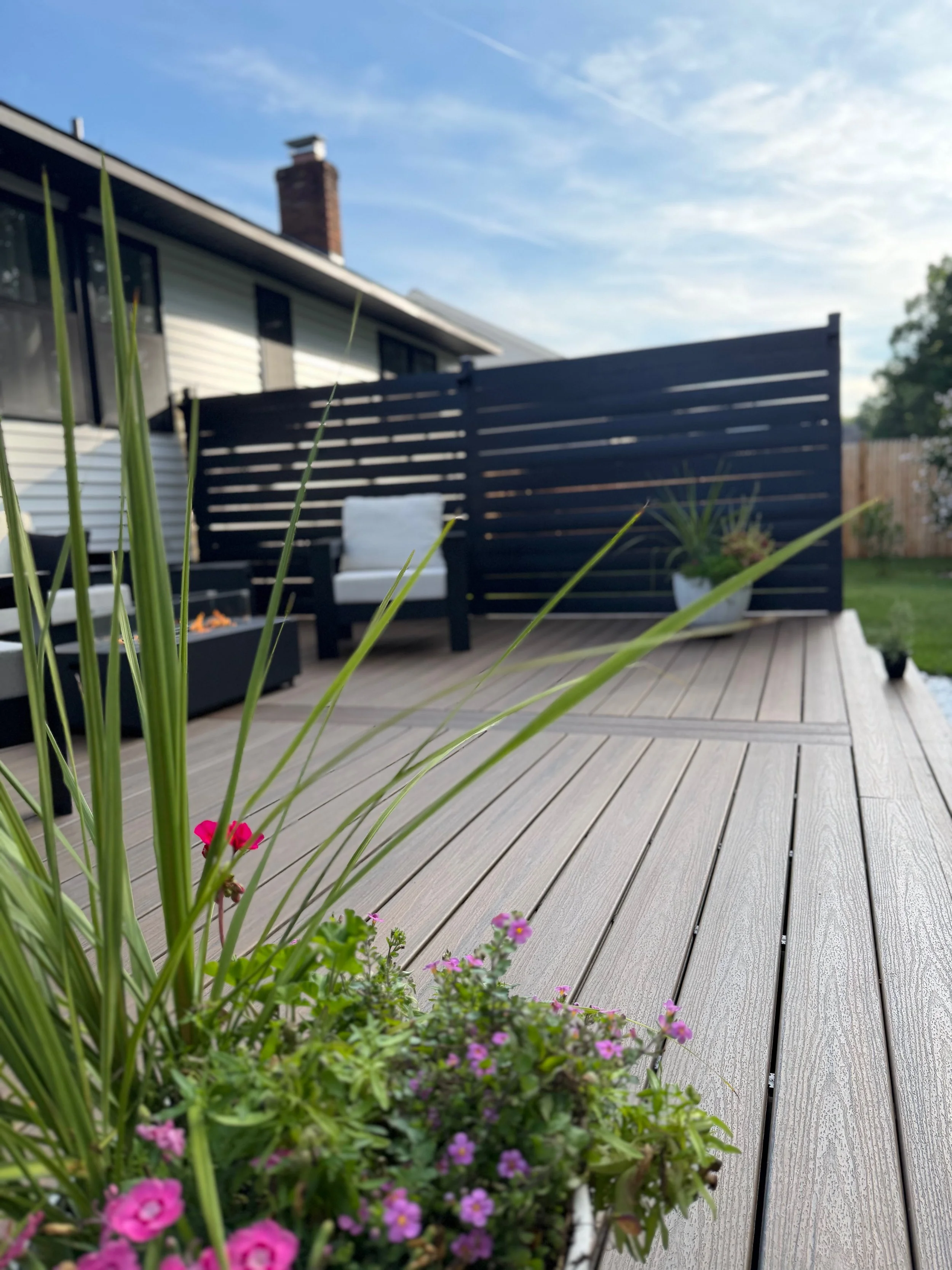 Close up of the finished Trex composite deck highlighting the clean decking lines, modern black privacy wall, and landscaped outdoor living space. The dark privacy wall ties in with the black new-construction windows for a cohesive, modern exterior d