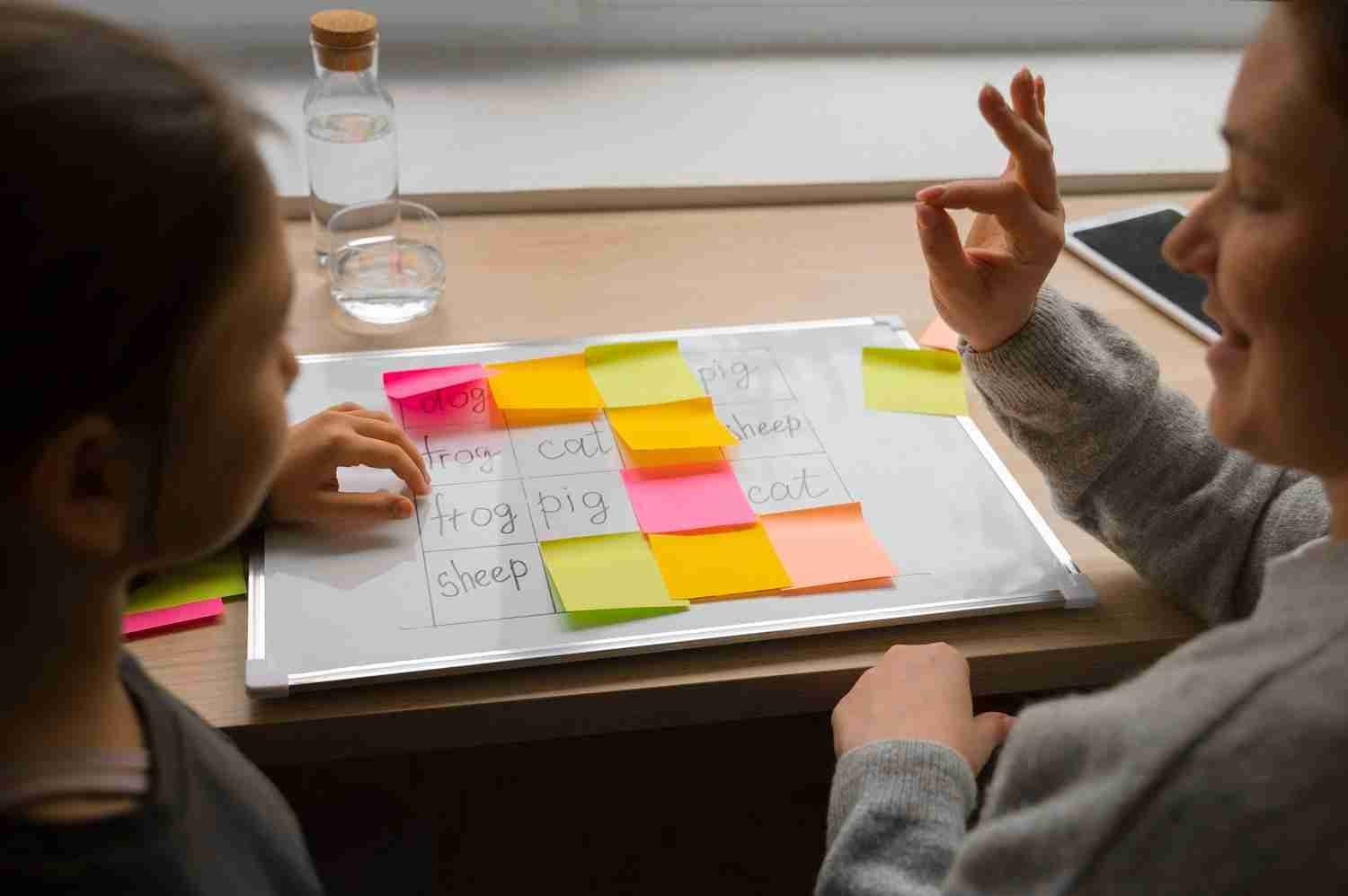 Two people using colored sticky notes on a whiteboard with animal names.