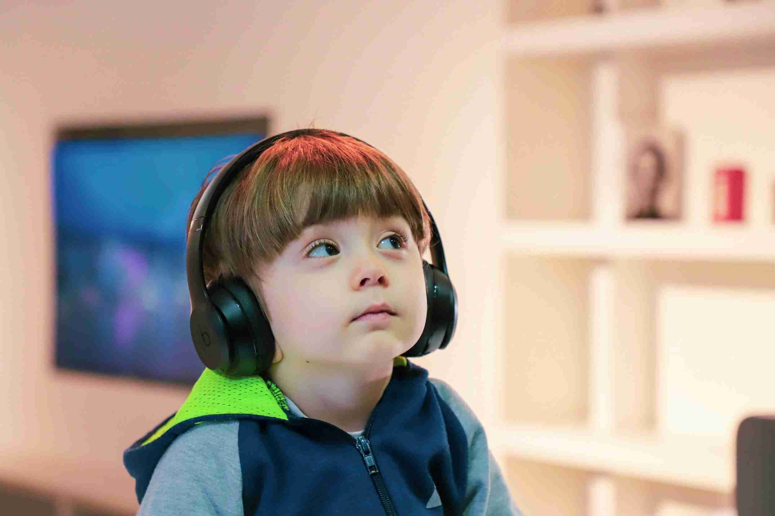 Young child wearing headphones, looking up in a room with soft lighting and blurred background.