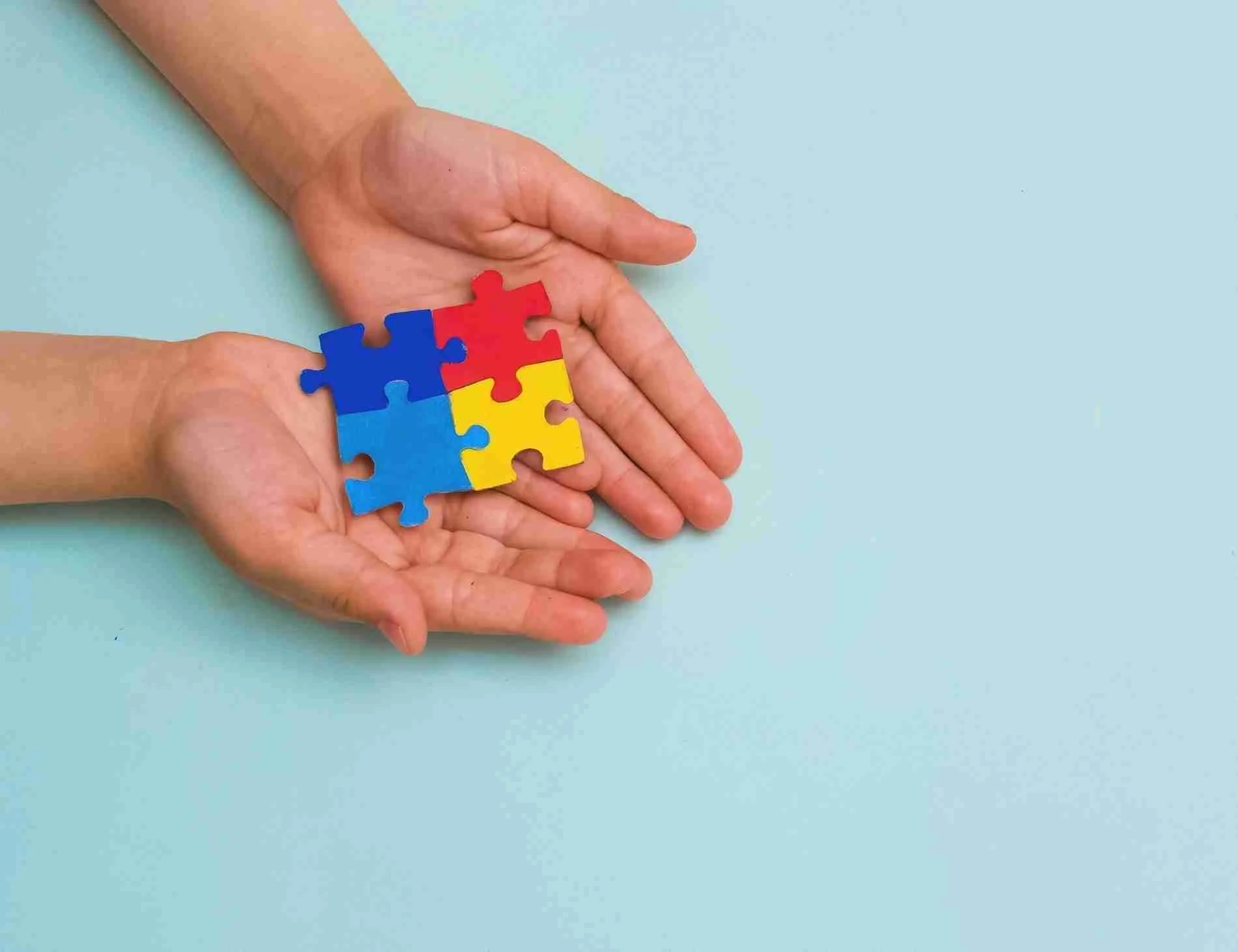Hands holding colorful interlocking puzzle pieces on a blue background.