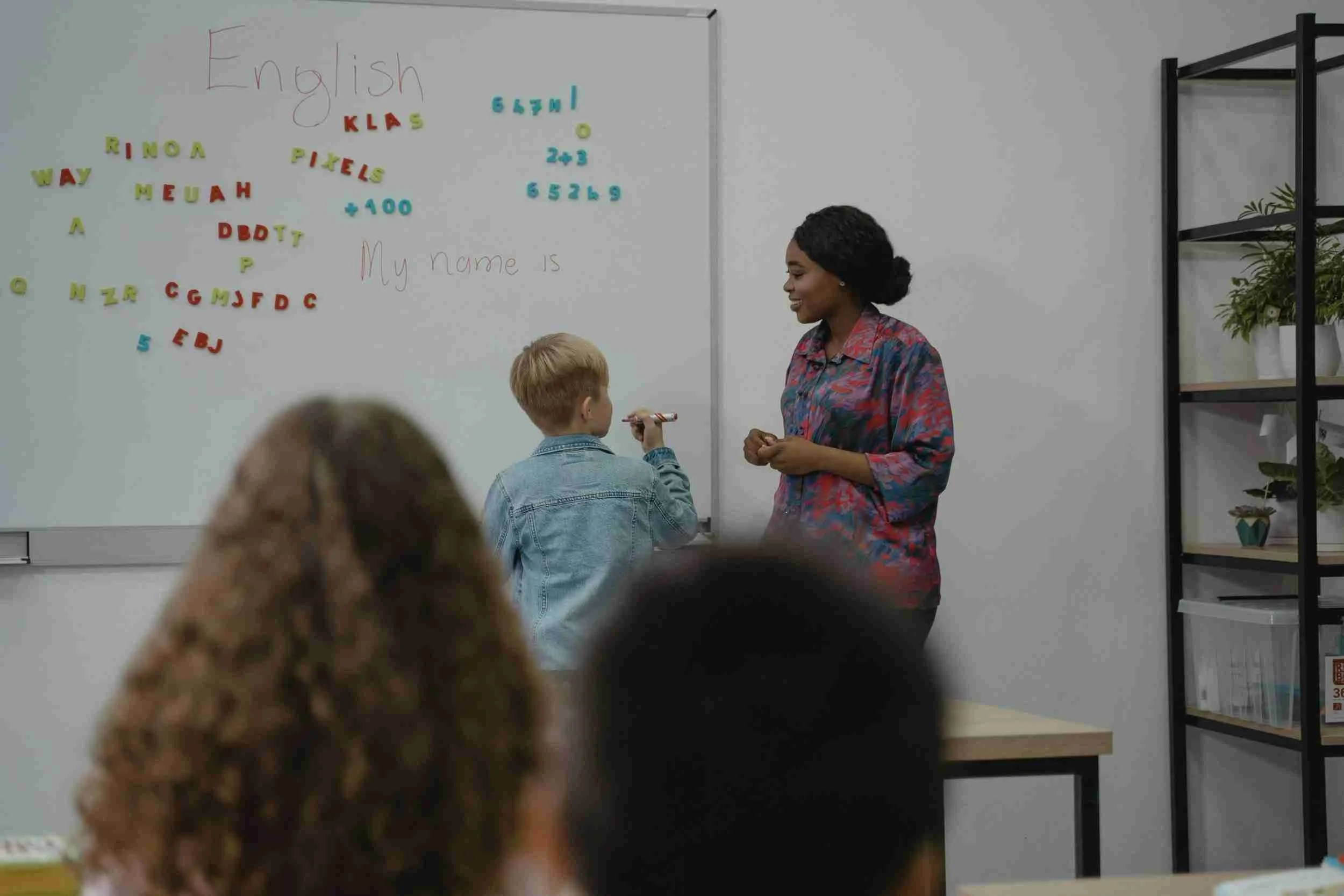 Teacher and student at whiteboard in classroom with magnetic letters and numbers.