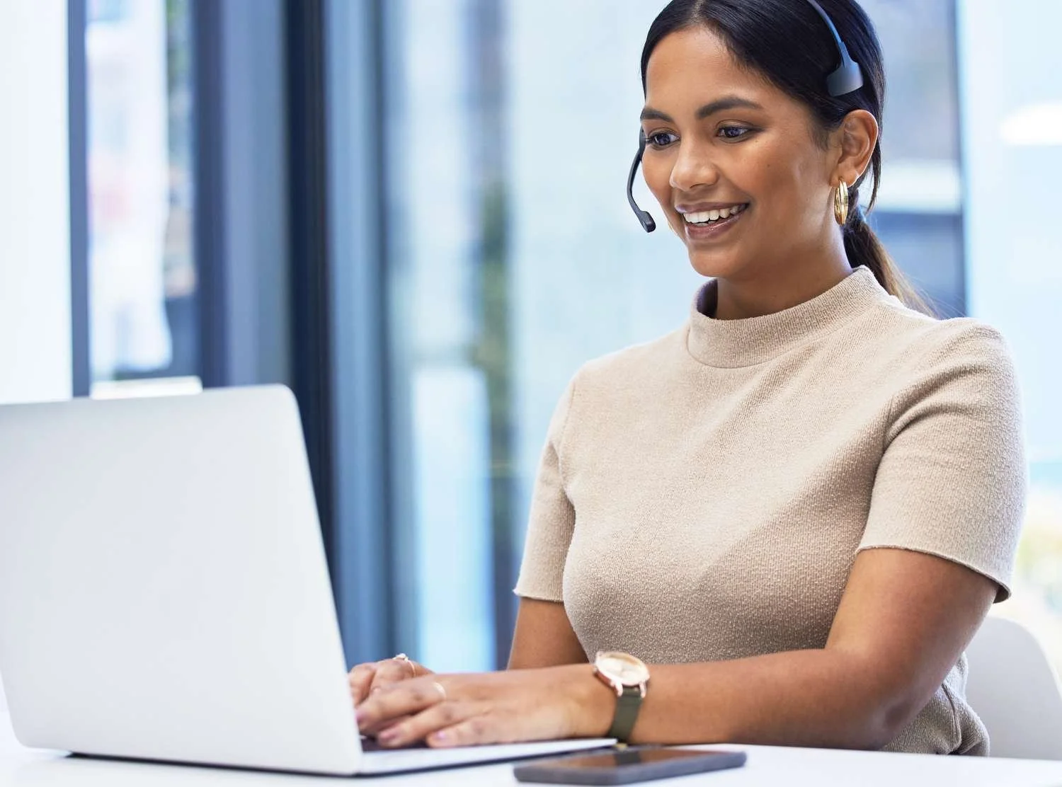 Woman with a headset working on a laptop in an office setting.