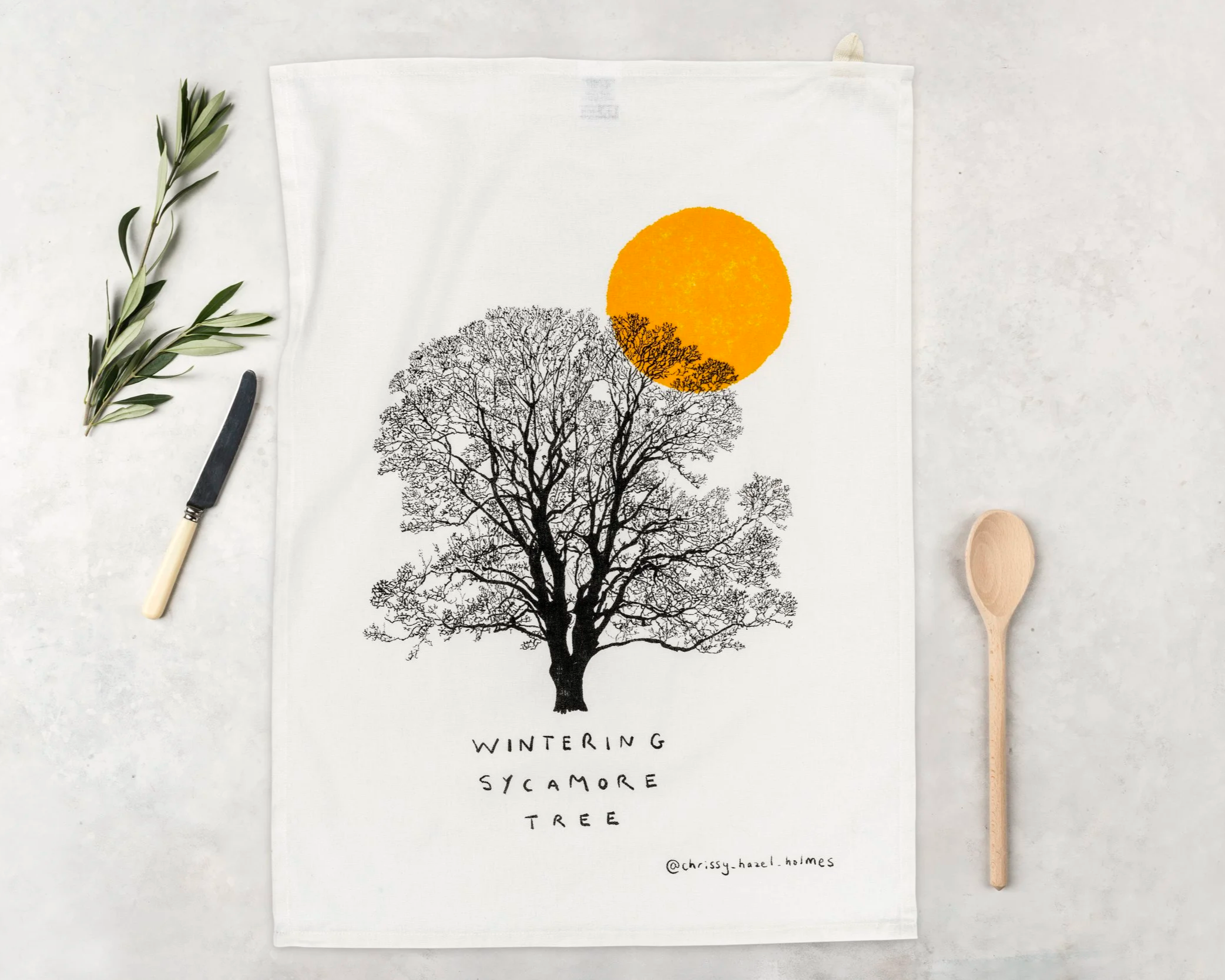 Artwork featuring a silhouette of a wintertime sycamore tree with an orange sun behind it, titled 'Wintering Sycamore Tree' and credited to @chrissy_hazel_hoimes, surrounded by a knife, spoon, and olive branch.