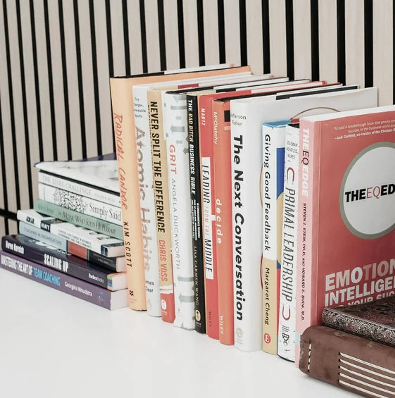 A collection of books on a white shelf, with various titles related to psychology, conflict resolution, emotional intelligence, and self-help, organized standing upright against a striped dark background for quick learn sessions.