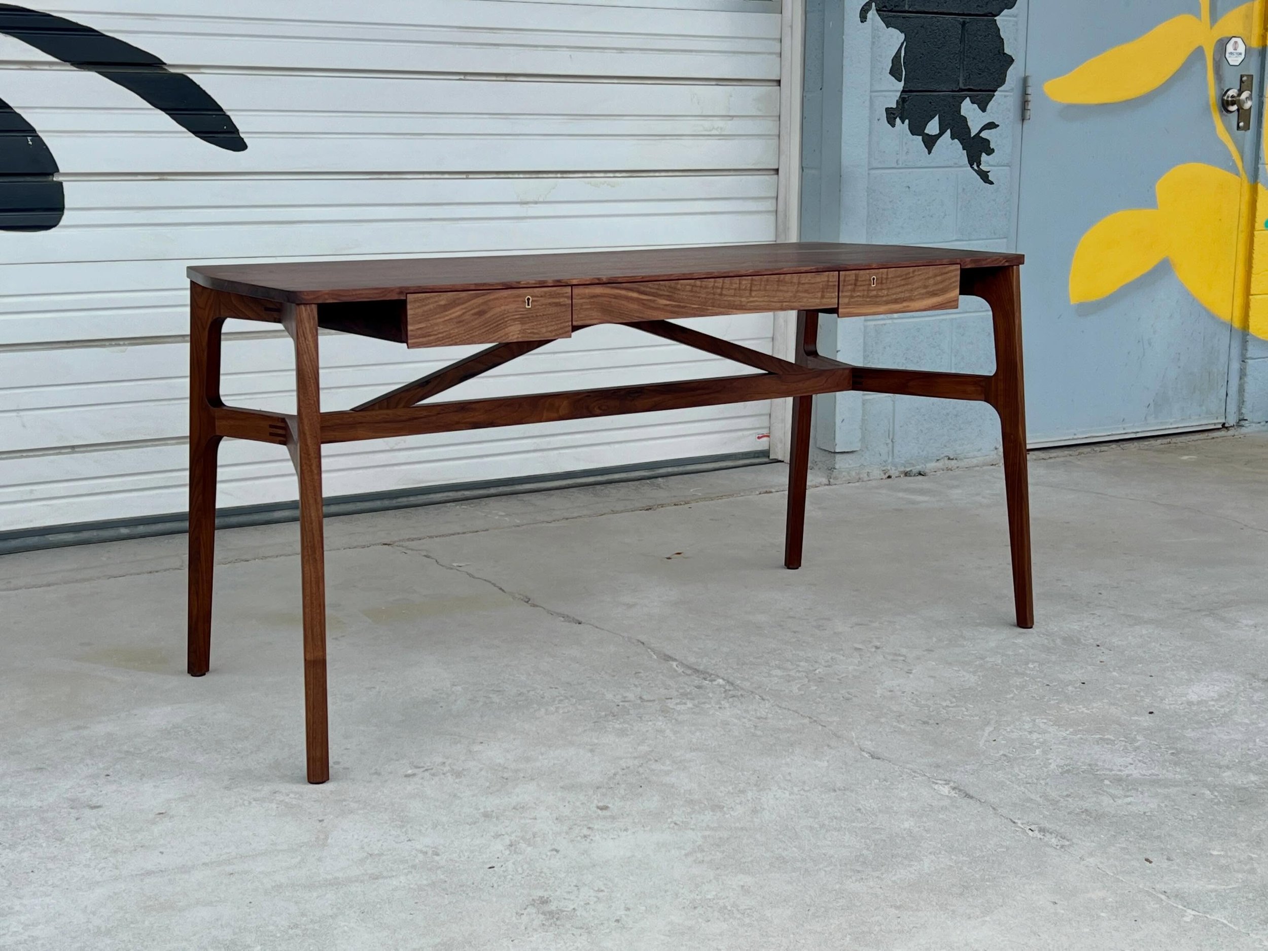 This is our Taper desk. It&rsquo;s built of solid walnut with three drawers, two of which lock via high quality brass hardware. It has some very cool joinery details in the legs and some really nice grain matched drawer fronts. The new version (comin