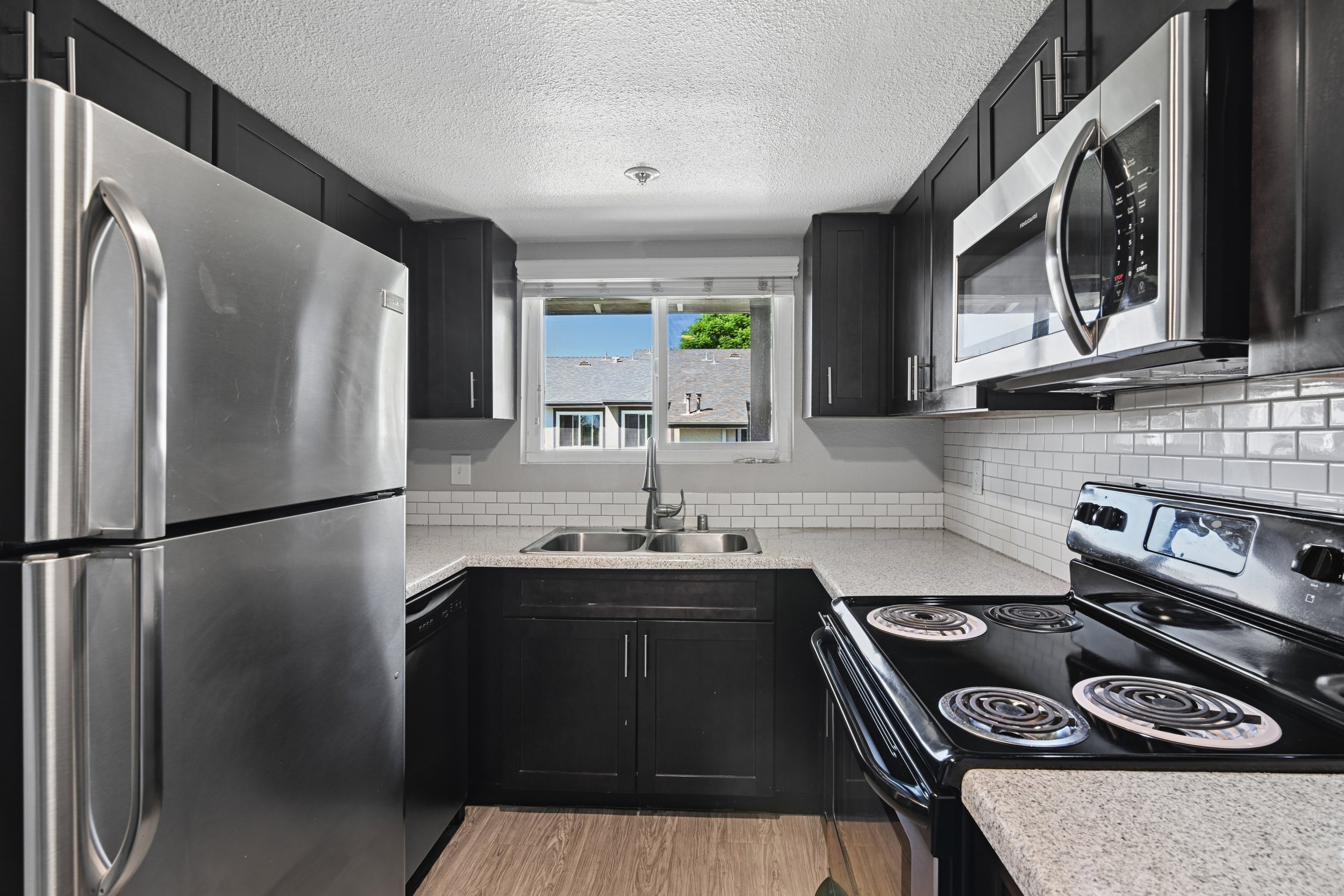 Kitchen in 1 Bedroom Citrus Heights Apartment homes with dark cabinetry, stainless appliances, and plank flooring for an elevated look. 