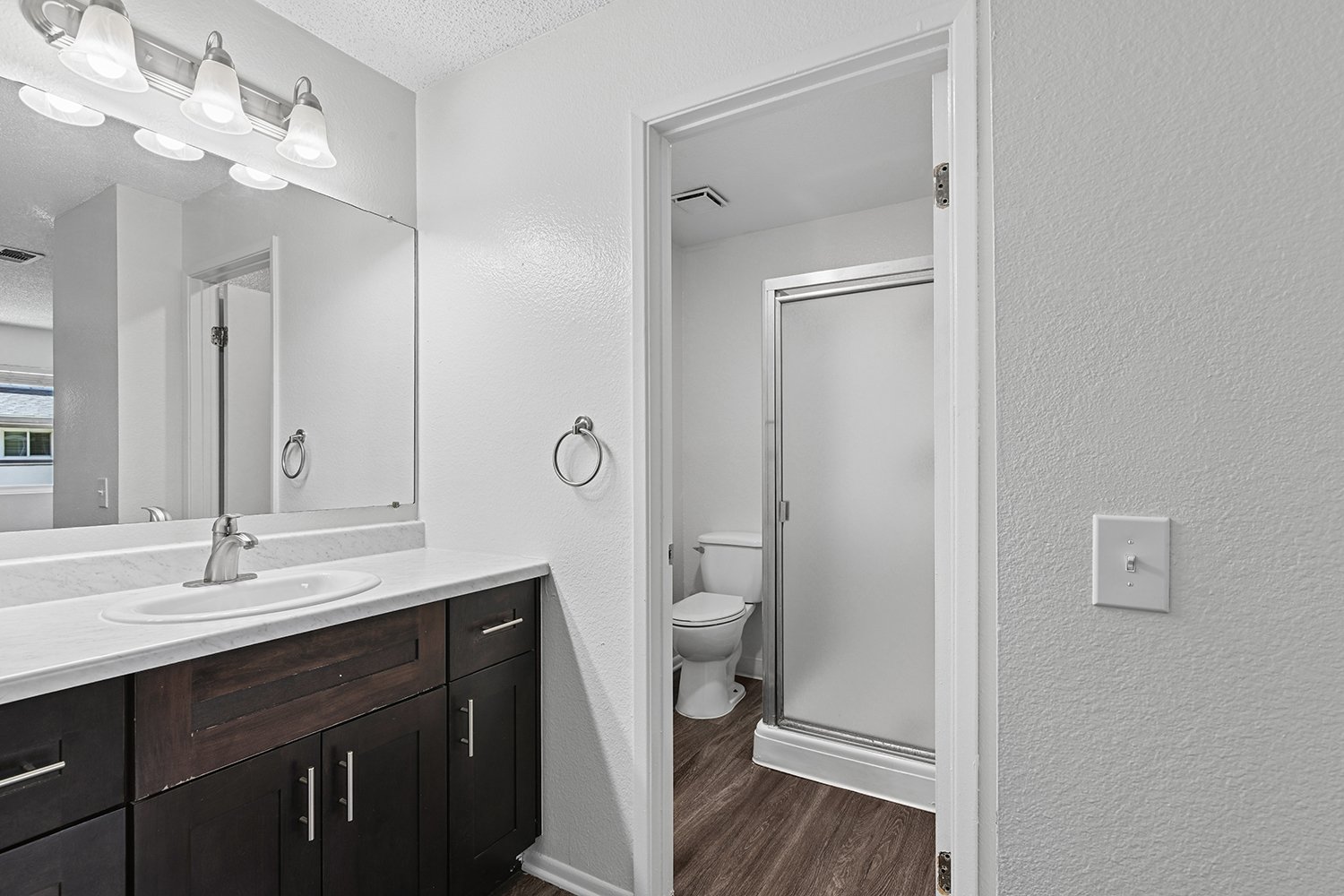 Private bathroom in Primary bedroom of Citrus Heights 3 Bedroom Apartment home with plank flooring, oversized vanity, quartz countertops and dark wood cabinetry.  