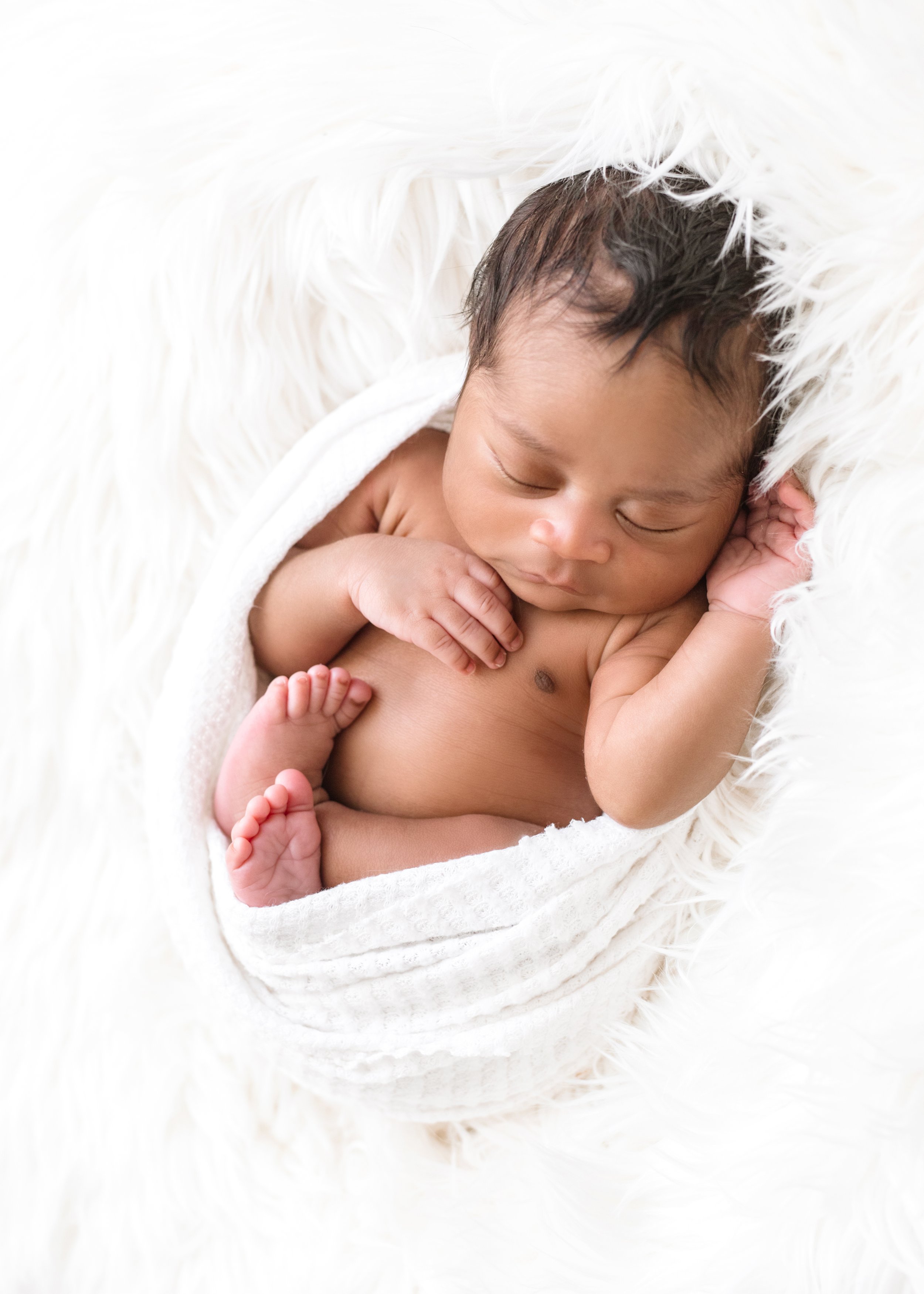 Sleeping newborn baby wrapped in a white blanket on a white fluffy surface.