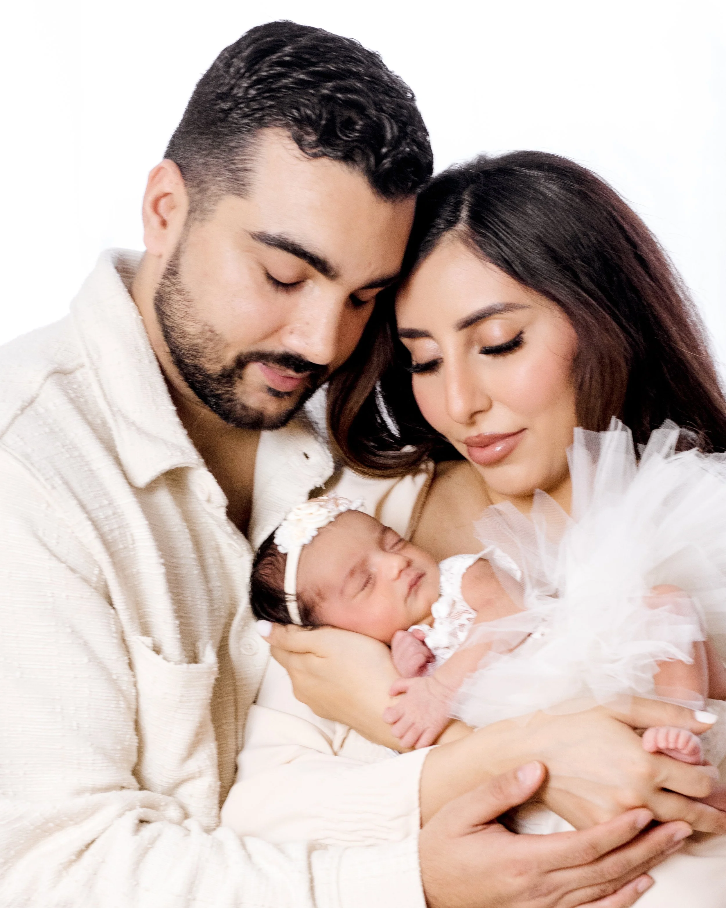 A couple holding their newborn baby, with their heads touching and eyes closed, in a close, intimate pose.