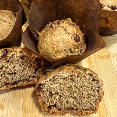 a cross section of a peanut butter, date, and banana muffin in front of a muffin in a liner