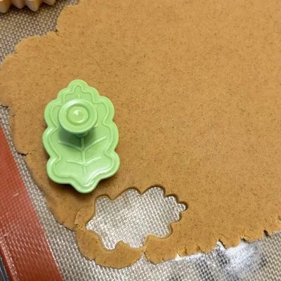 brown sugar cookie dough rolled out and it is being cut with a leaf shaped cookie cutter
