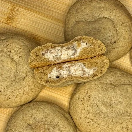 caramel apple cheesecake cookies on a wooden cutting board. one is split in half so you can see the filling