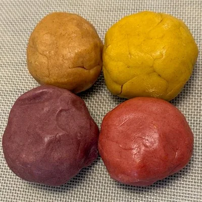 balls of cookie dough colored brown, yellow, purple, and red