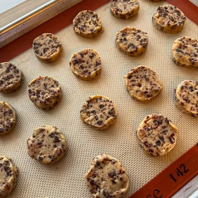 circular slices of cherry chocolate almond cookie dough on a cookie sheet