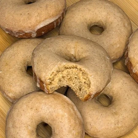 apple cider glazed donuts on a wooden cutting board and one donut has a bite taken out of it