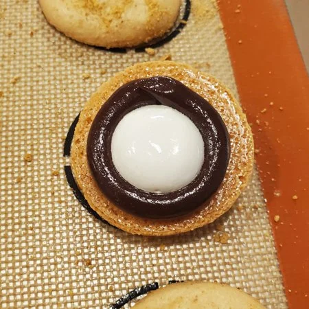 open faced s'mores macaron showing filling of marshmallow fluff surrounded by chocolate ganache
