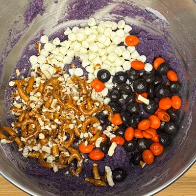 purple cookie dough with white chocolate chips, orange and black M&Ms, and pretzel pieces