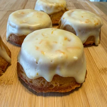 carrot orange tea cakes with orange cream cheese icing on a wooden cutting board