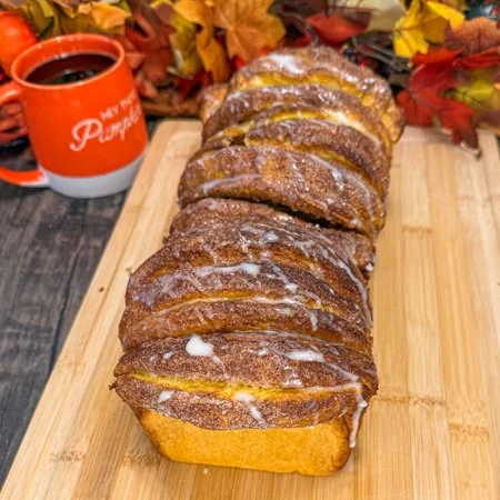 pumpkin pull apart bread on a wooden cutting board with an orange mug and leaves in the background
