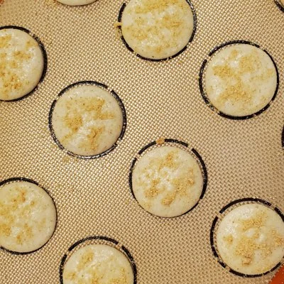 unbaked smores macaron shells piped on a silicone baking mat with graham cracker crumbs sprinkled on top