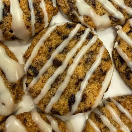 close up of cherry chocolate almond cookies with white chocolate icing on a white plate