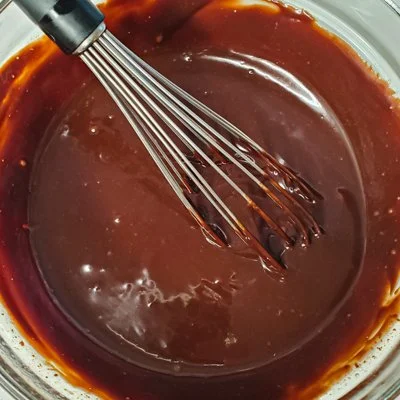 chocolate ganache in a clear bowl with a whisk