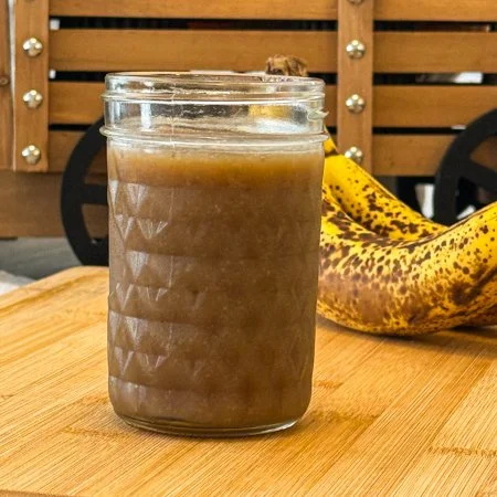 banana caramel in a glass jar on a wooden cutting board with bananas sitting in the background