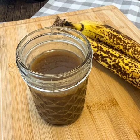banana caramel in a glass jar on a wooden cutting board with two bananas