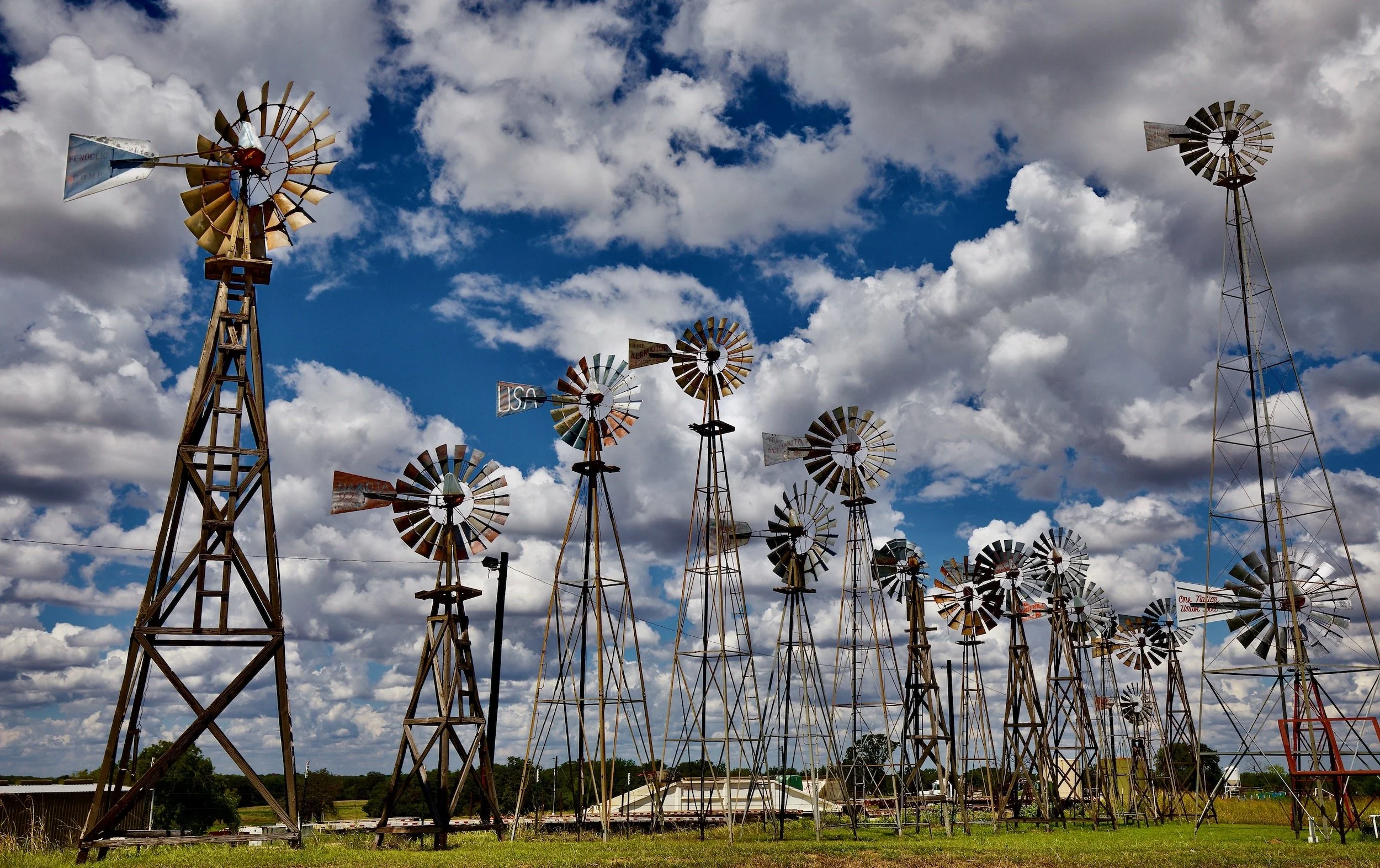 " Windmill Reunion " Collection of historic Texas windmills beneath dramatic clouds and blue skies.
