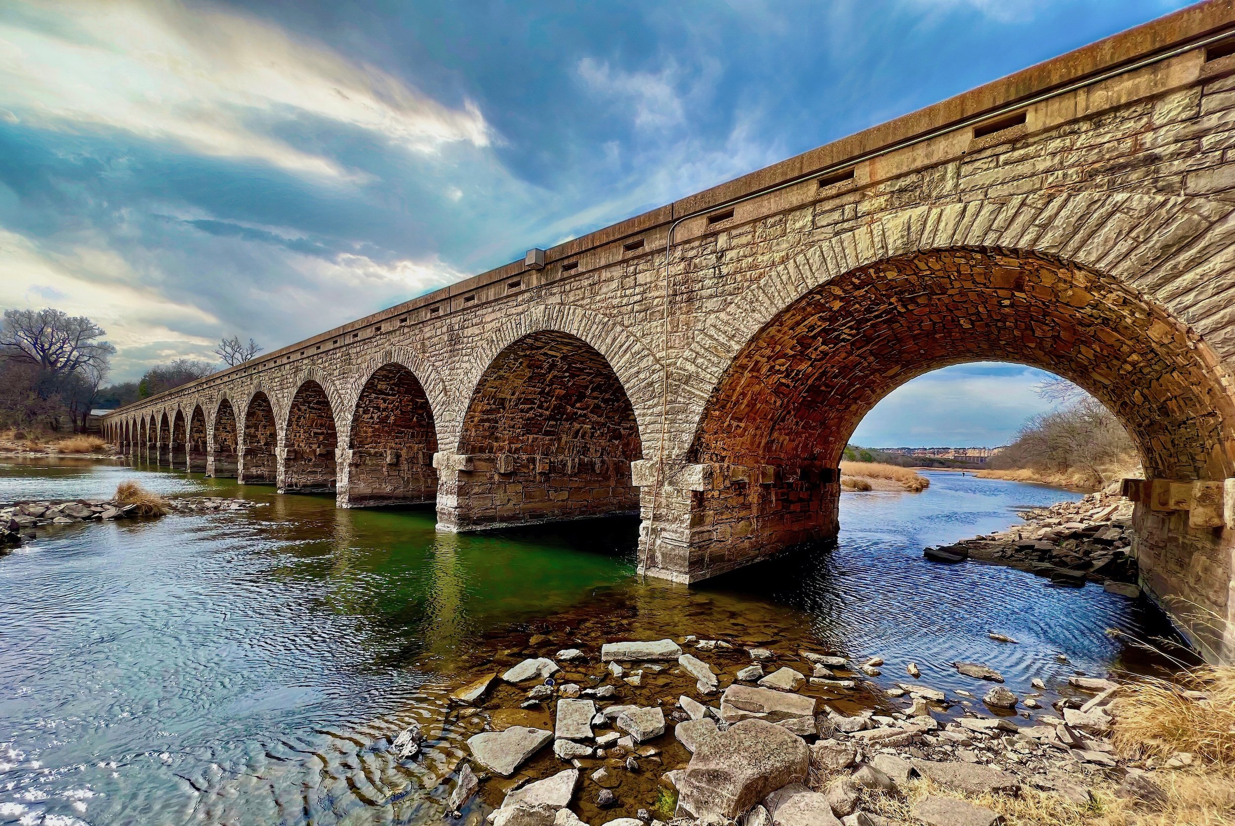 "Timeless Passage"Historic stone bridge spanning tranquil waters beneath dramatic skies