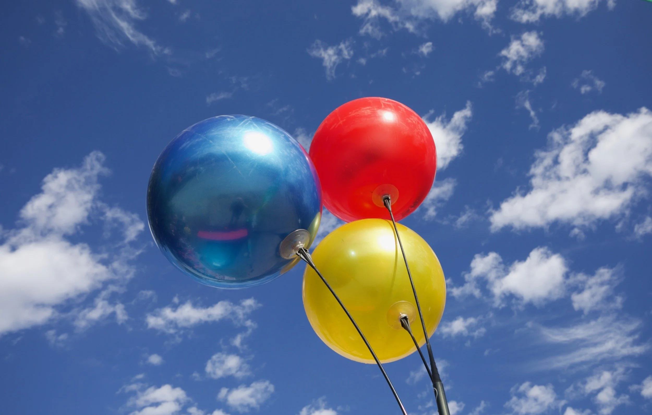 " Color Theory " Red, Blue, and yellow balloons floating beneath brilliant skies and scattered clouds.