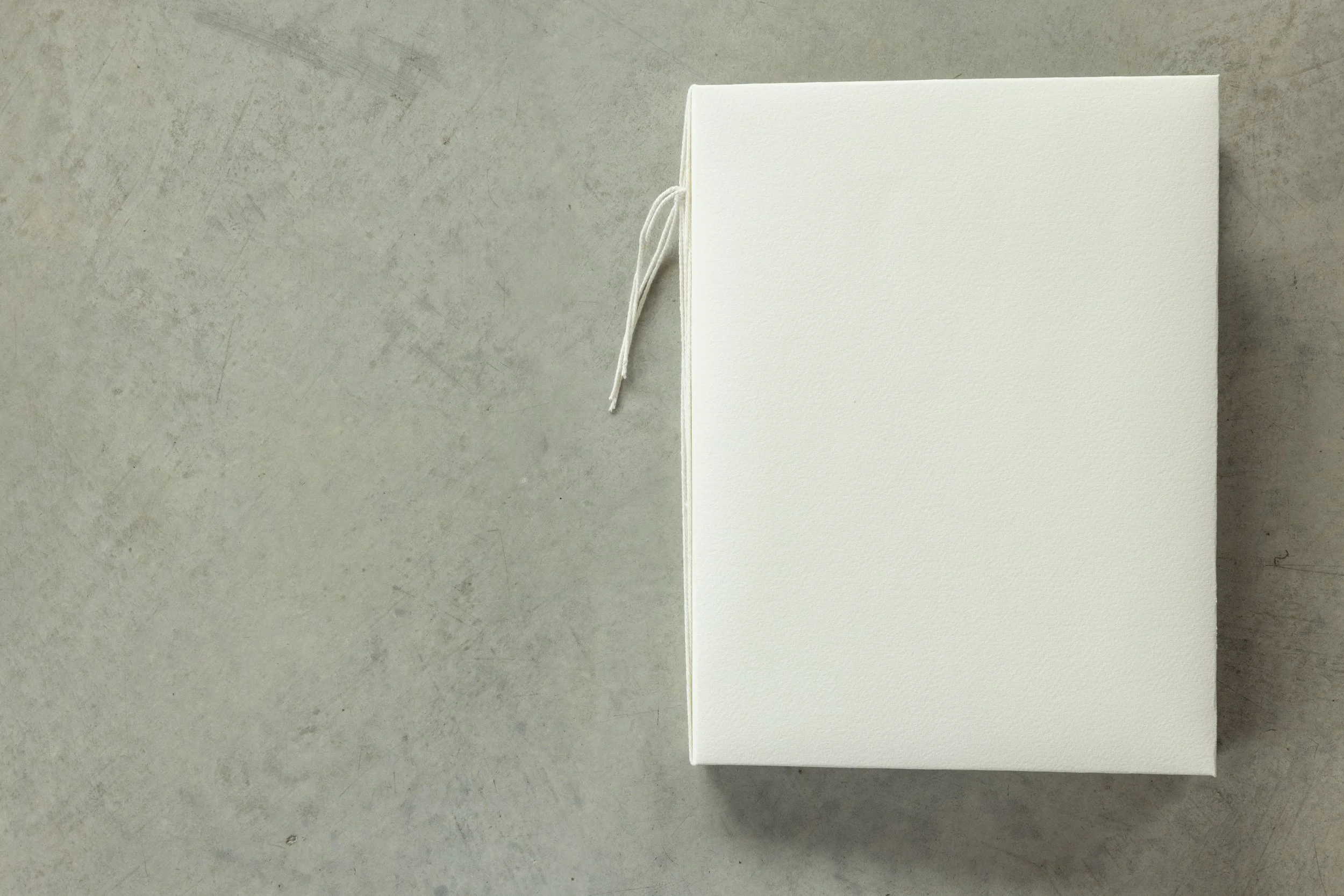A plain white closed box with a textured surface sitting on a concrete surface next to a white material with a string attached.