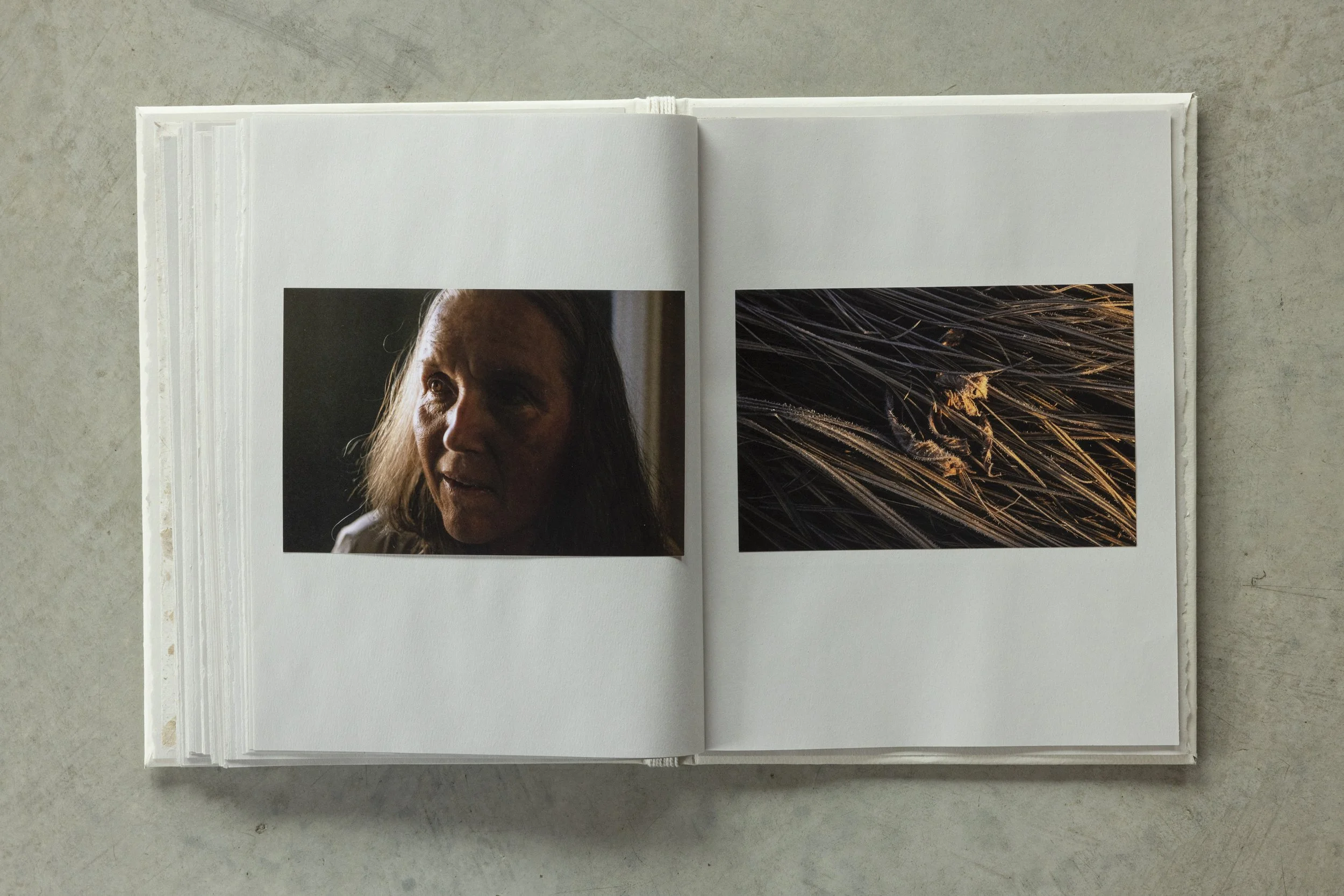 Open book on a gray surface displaying a portrait of a woman with long hair on the left page and close-up of grass or plant detail on the right page.