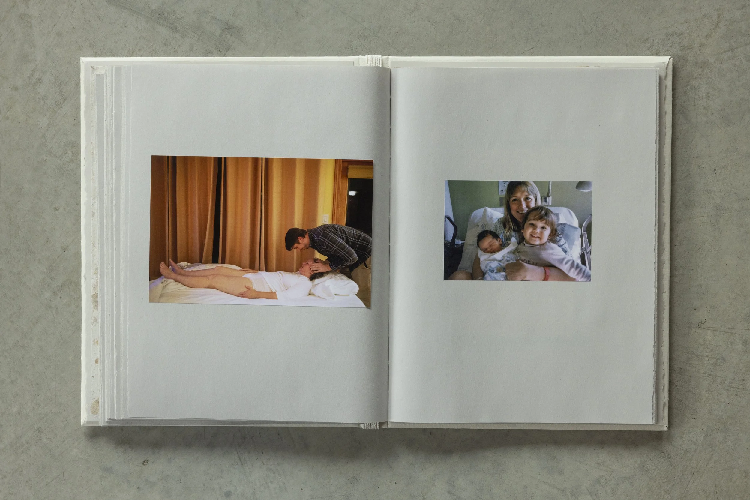 Open photo album showing two printed photographs on a page, lying on a concrete surface.