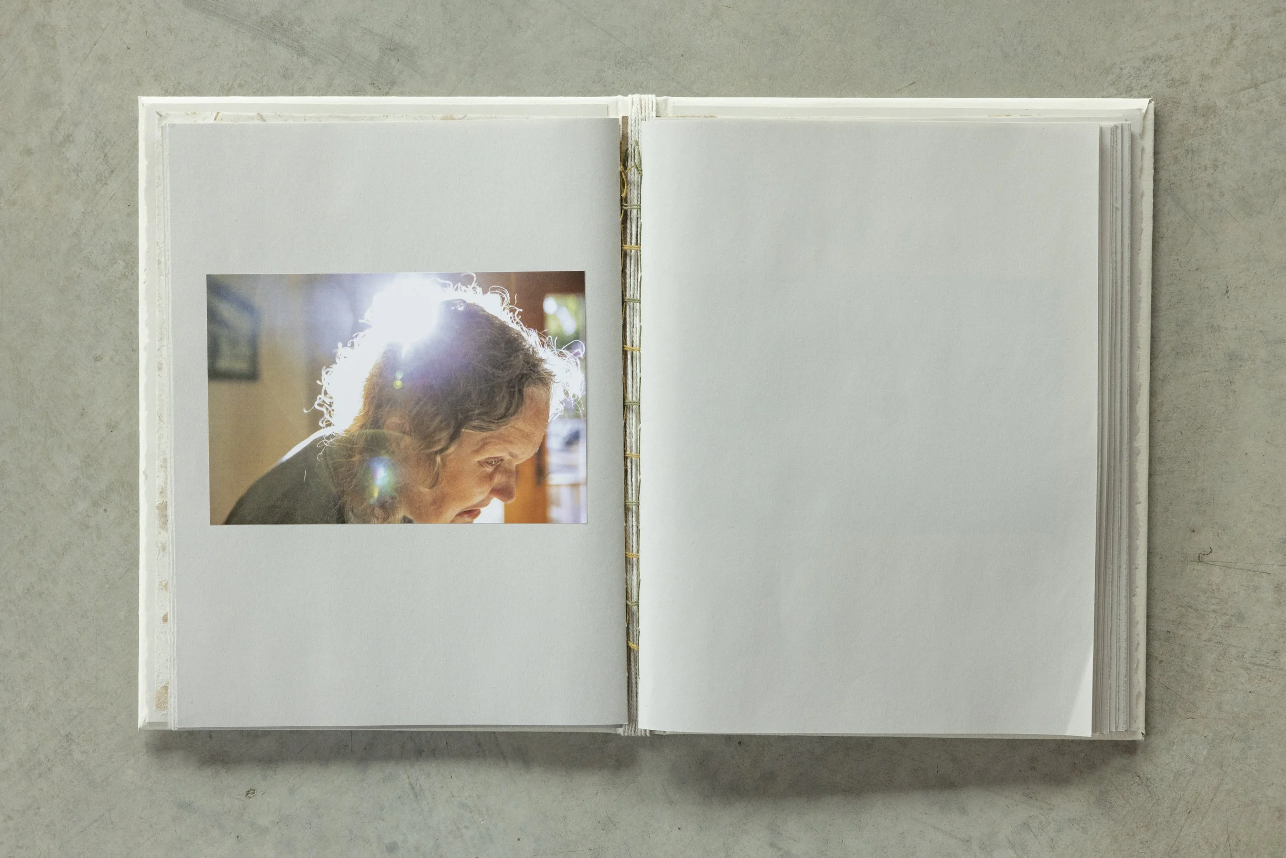 Open photo album with blank white pages and a small photograph of an elderly woman with curly hair, lit from behind, on the left page.