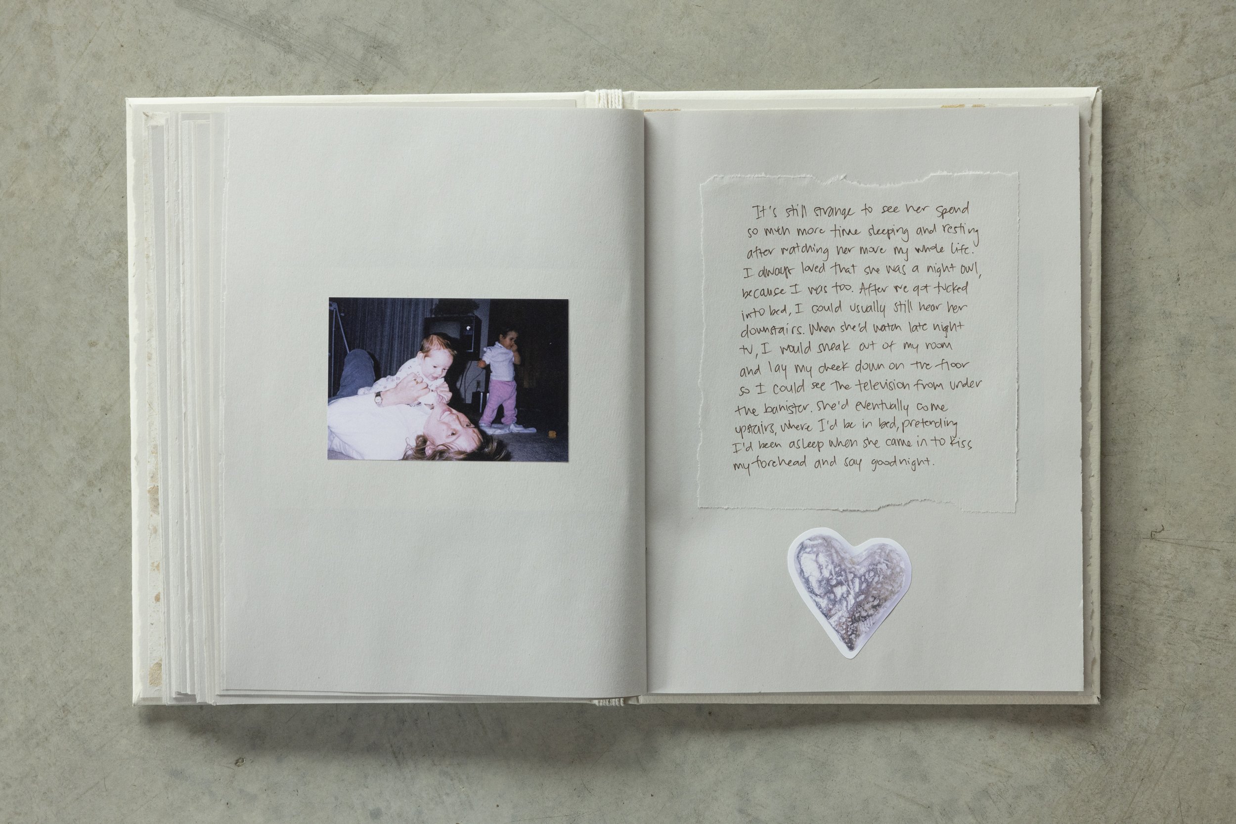 Open scrapbook with handwritten note on the right page and a photo of children on the left page, placed on a light-colored surface.