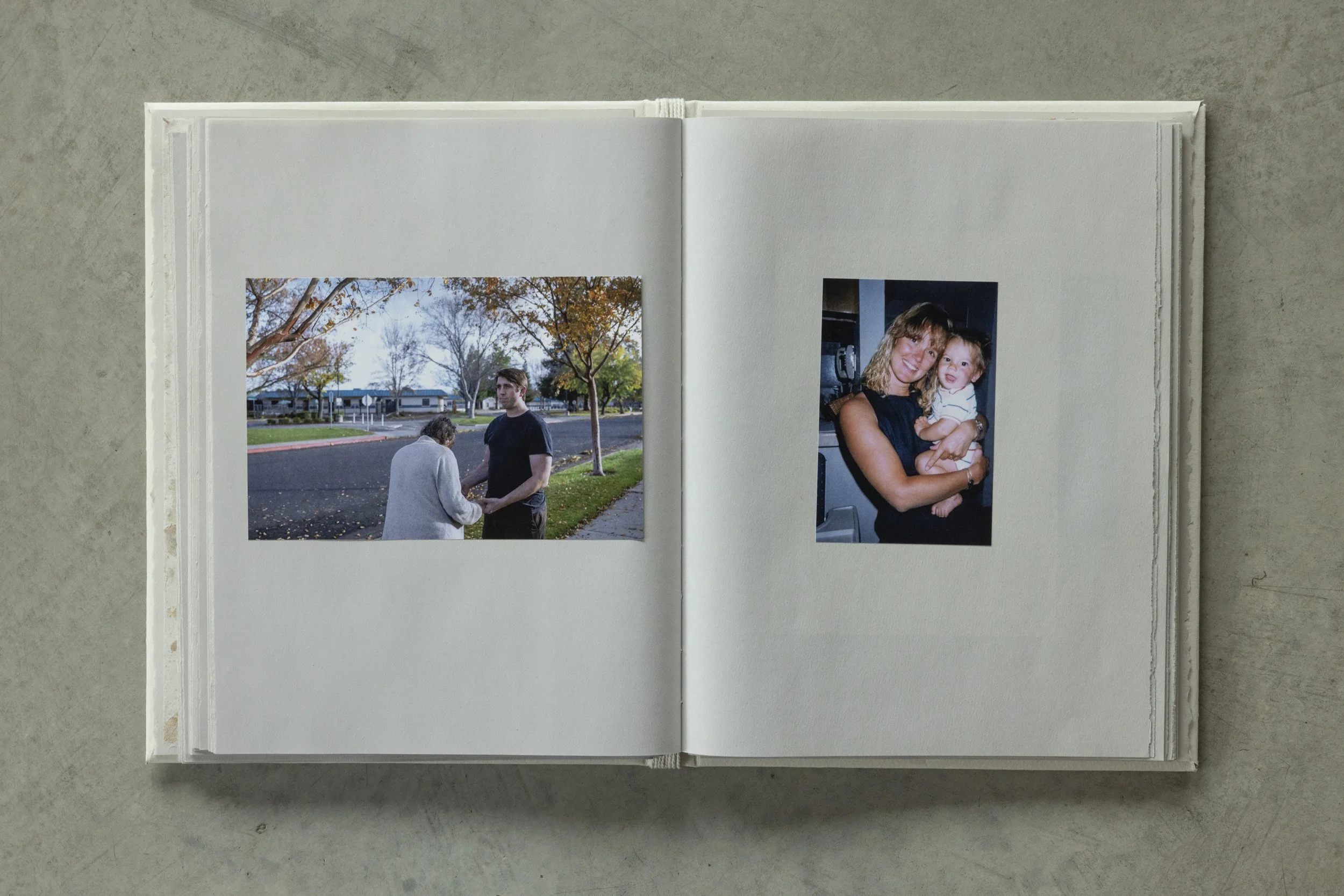 Open scrapbook or photo album with two printed photographs on white pages, placed on a concrete surface.