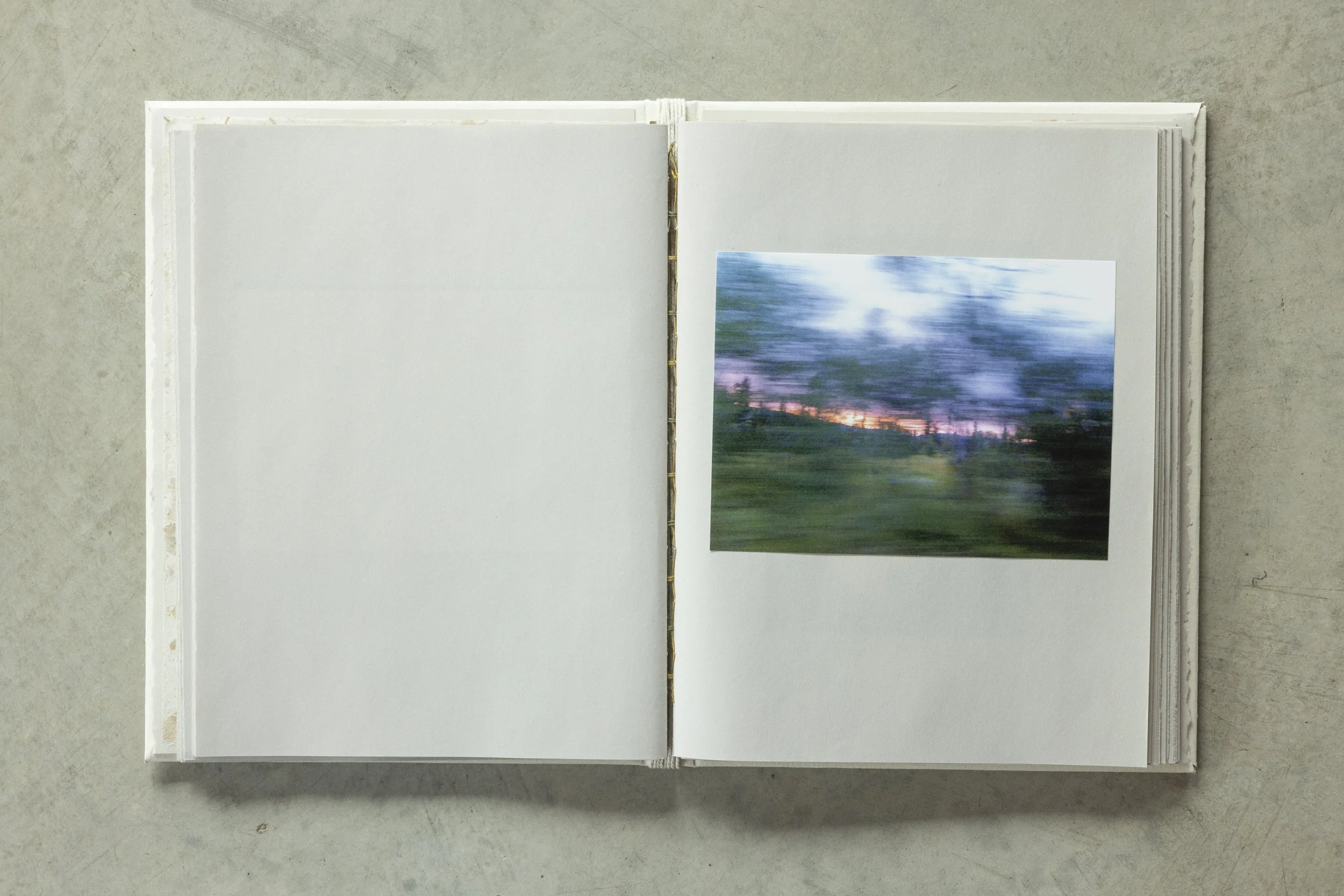 Open notebooks with blank white pages and a landscape photograph of a sunset over a field attached to one page.