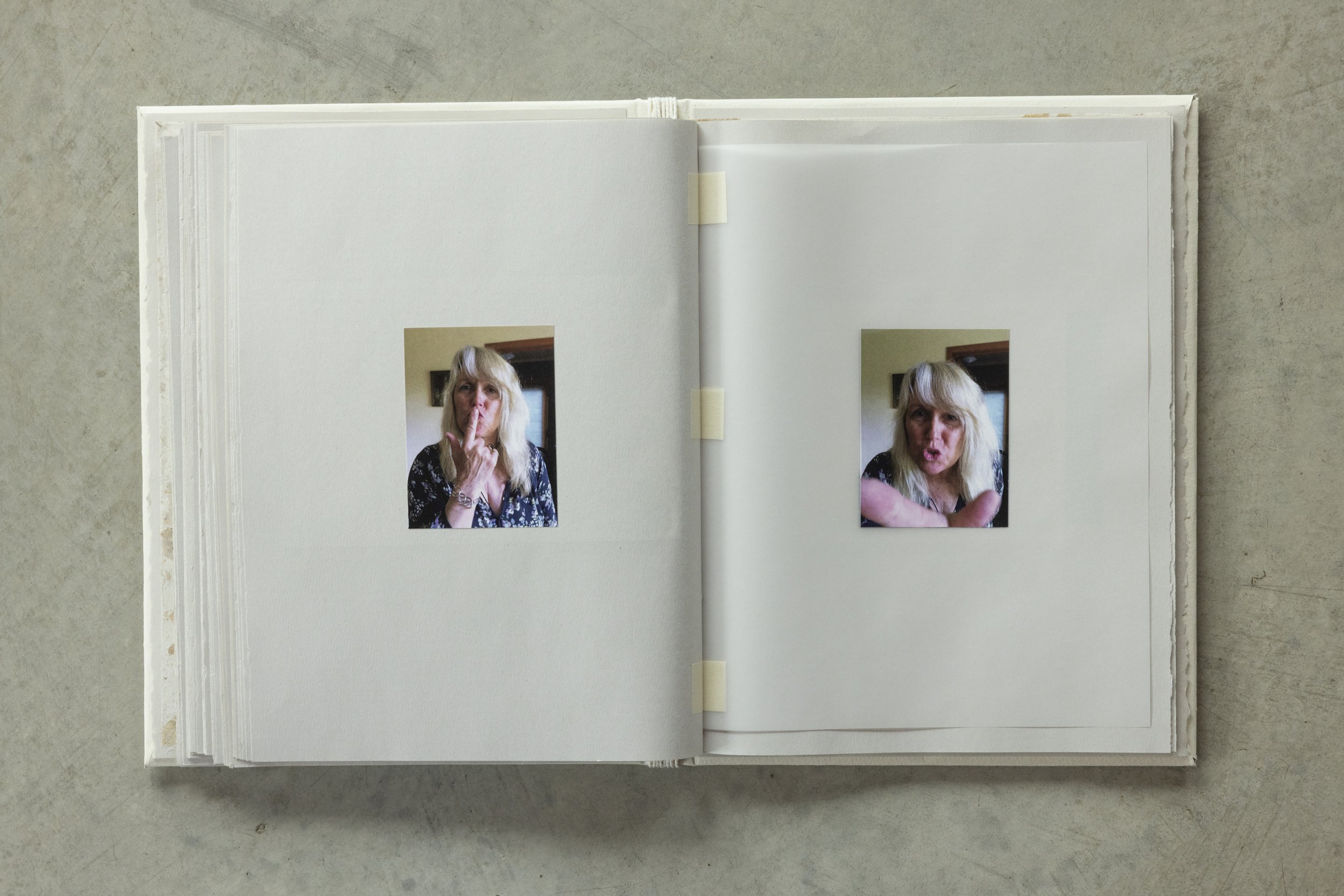 Open notebook with two photographs of a woman making expressive gestures, lying on a flat surface.