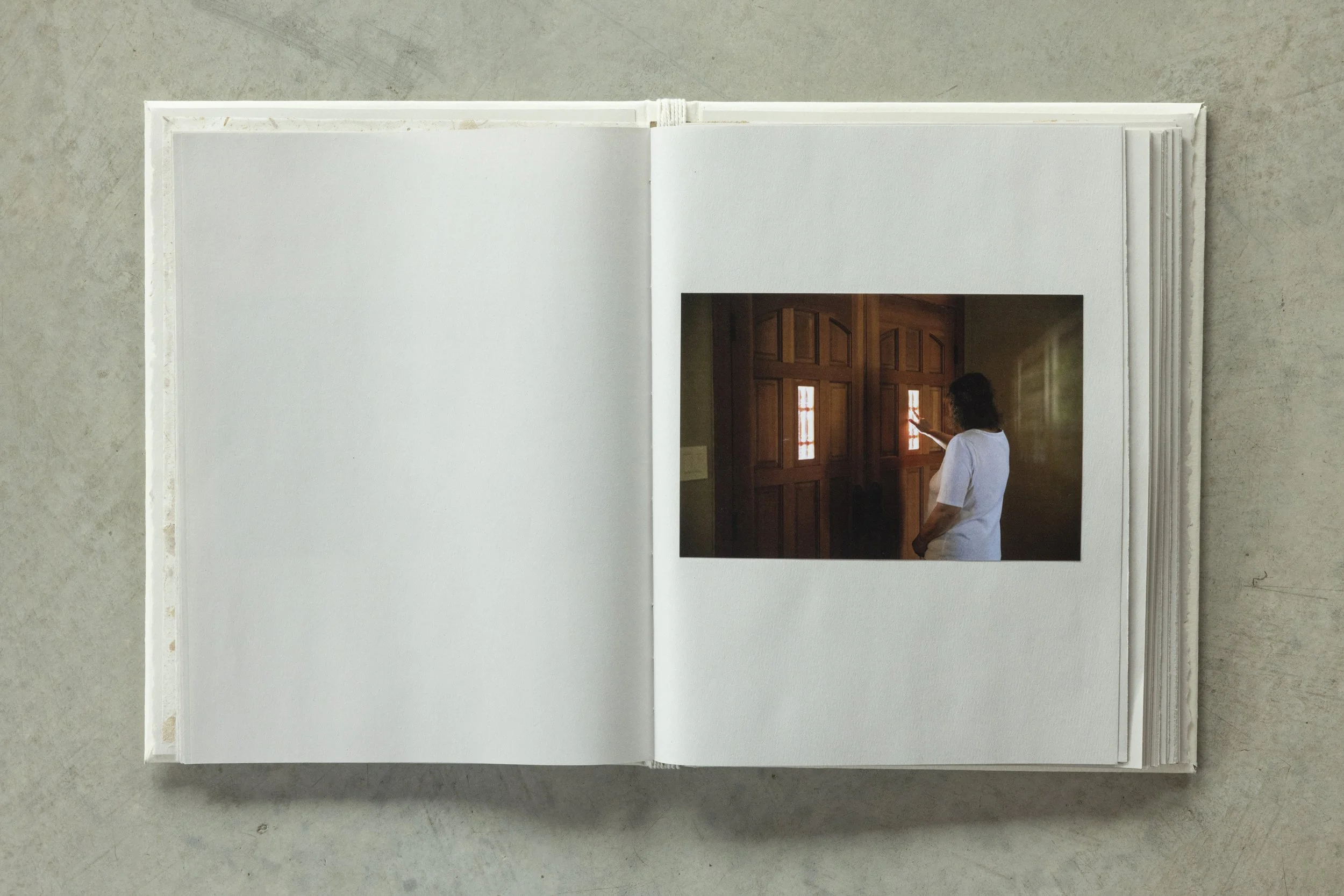 An open photo album on a light-colored surface showing a photo of a woman in a white t-shirt touching a wooden door with small windows.
