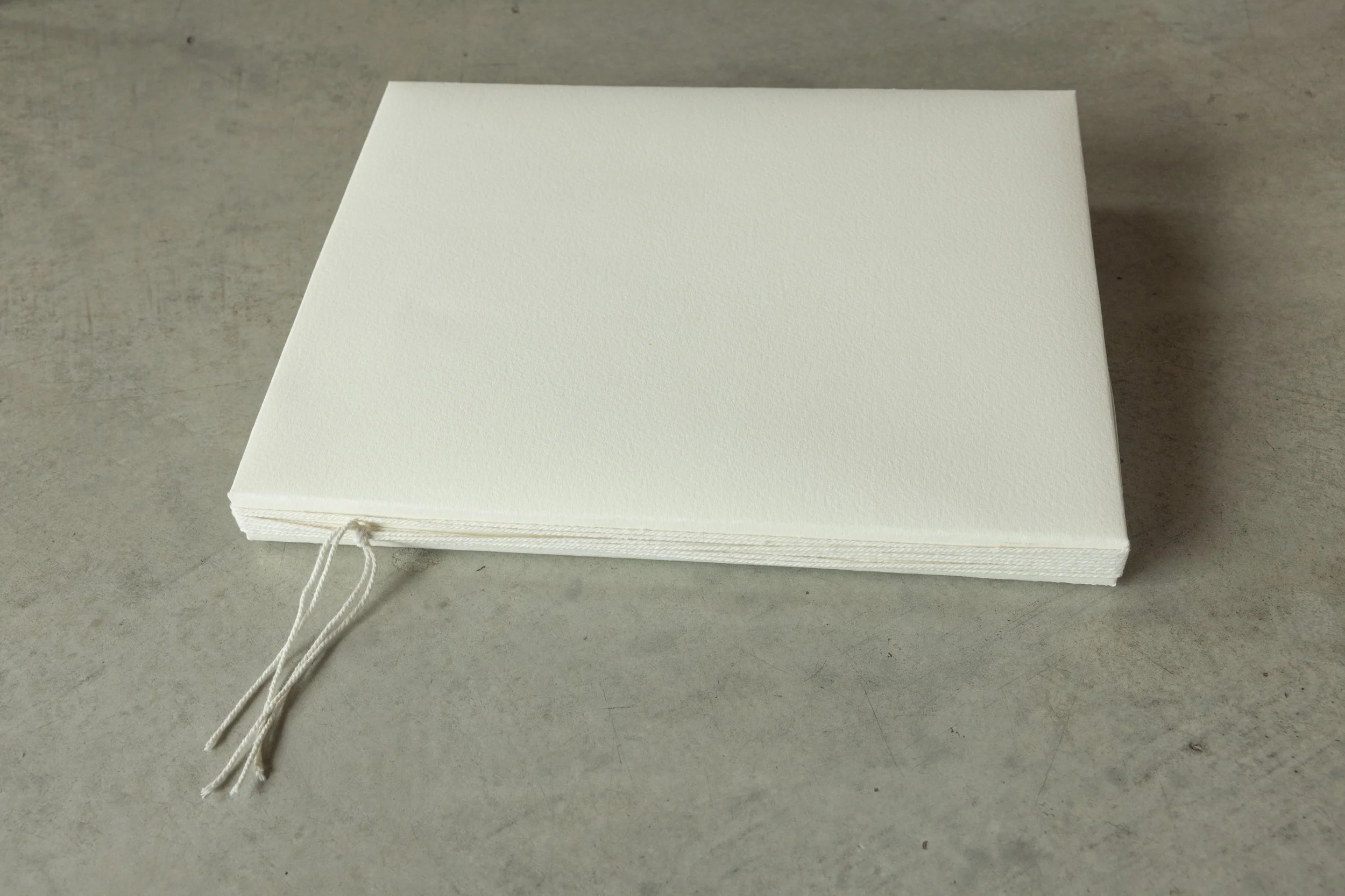 A stack of white paper sheets bound with a string tied in a bow, placed on a gray surface.