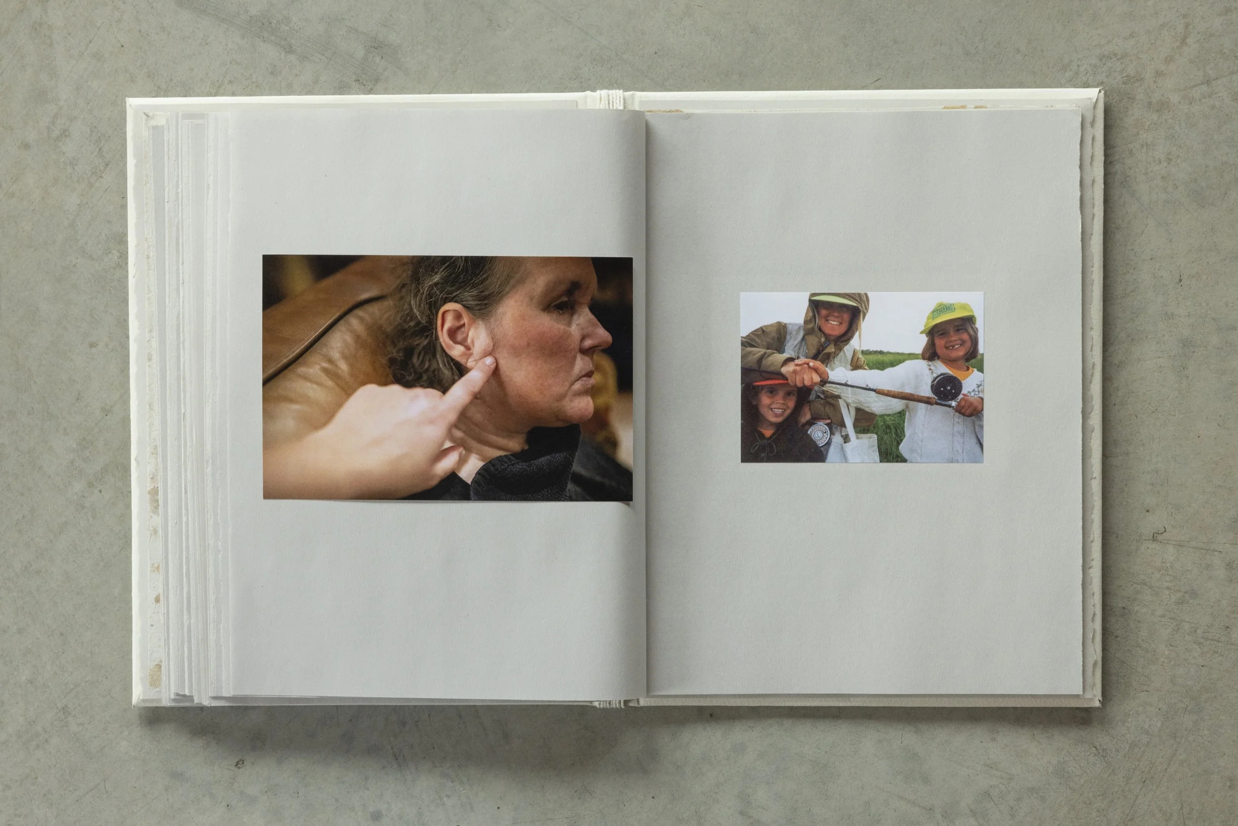 Open photo album on a flat surface showing two photos: one of a woman touching her face, and another of children outdoors in hats holding a fishing rod.