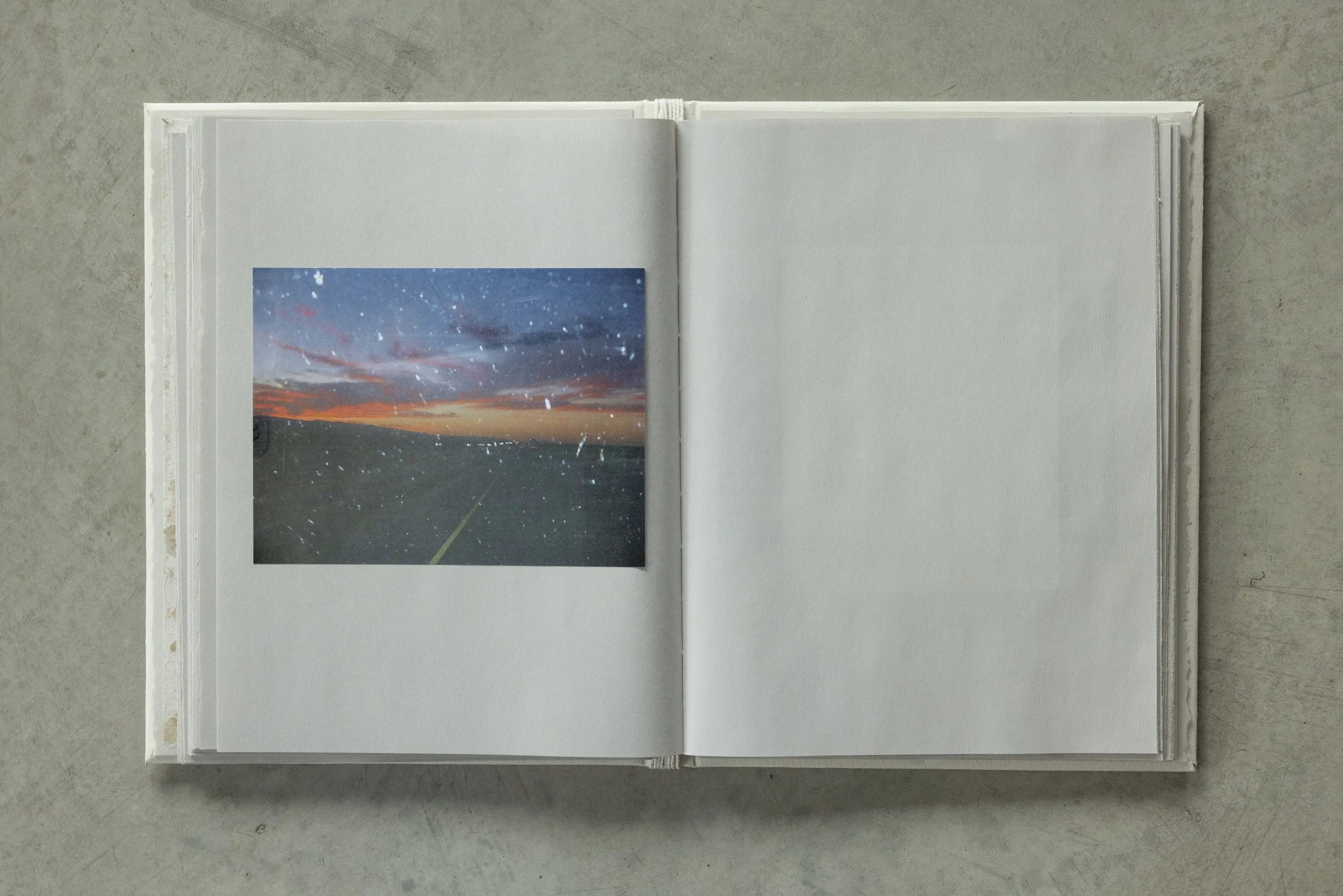 Open white photo album displaying a photograph of a colorful sunset over a body of water with a starry sky.