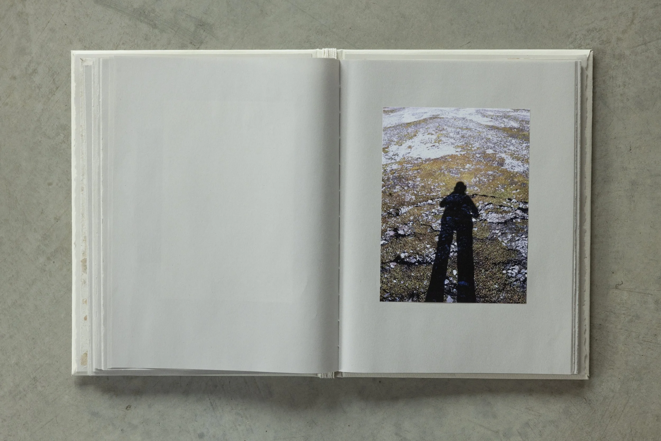 Open photo album or journal with a photograph of a shadowed person walking on rocky terrain with patches of snow.