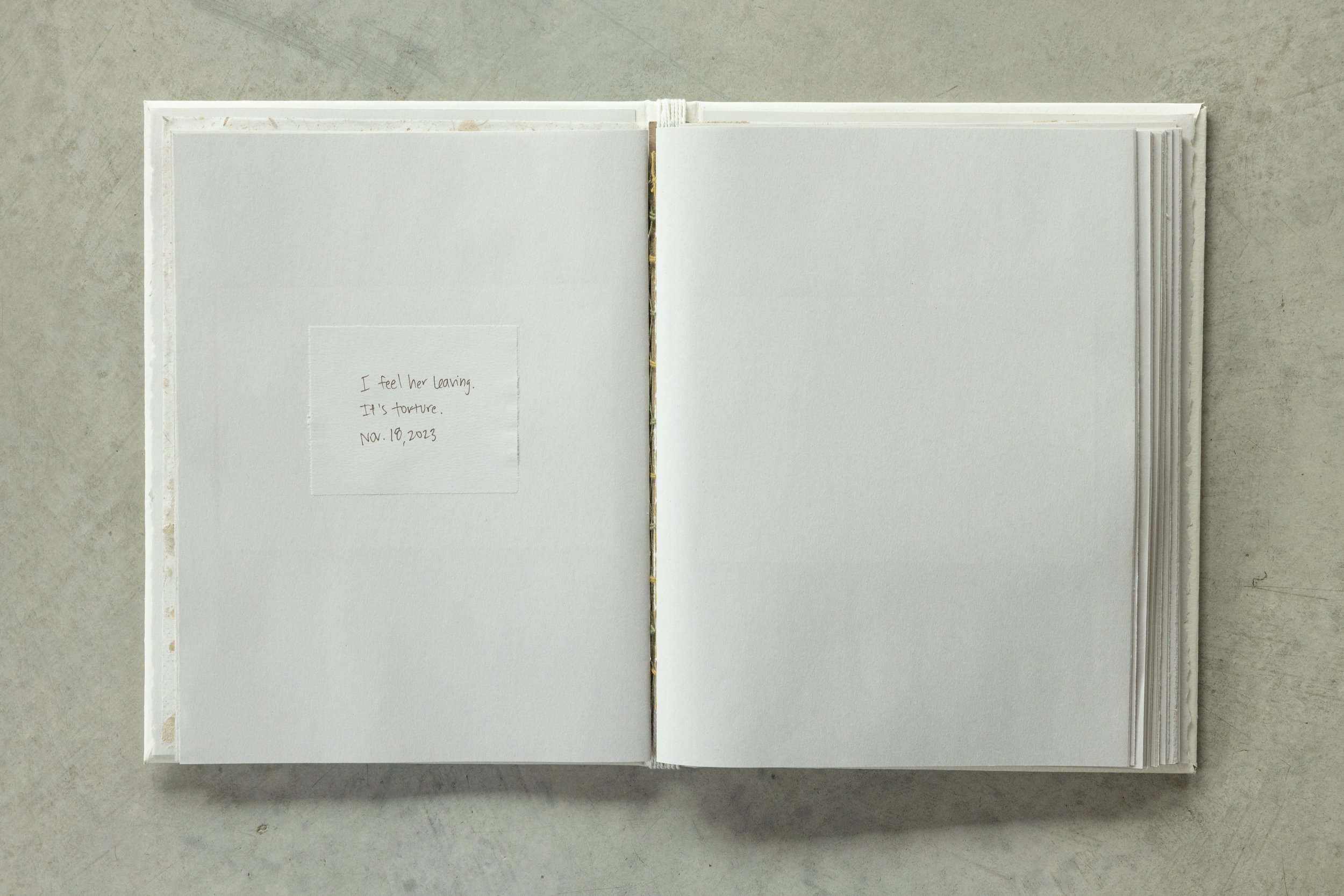 Open blank sketchbook with handwritten note on left page, lying on a gray surface.